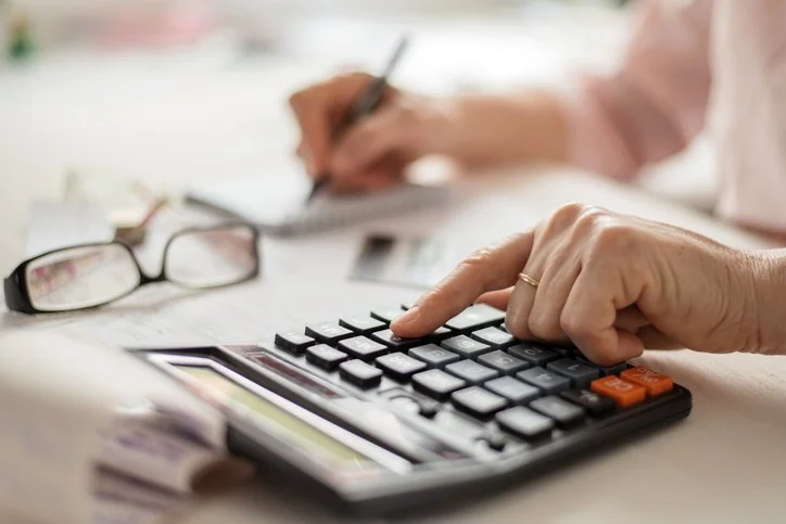 Person using calculator on a desk and writing in notebook