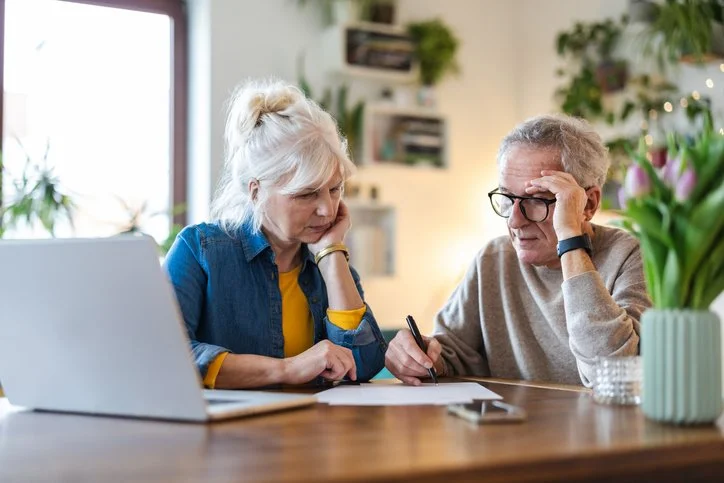 Senior couple sitting at table, looking over paperwork, looking serious