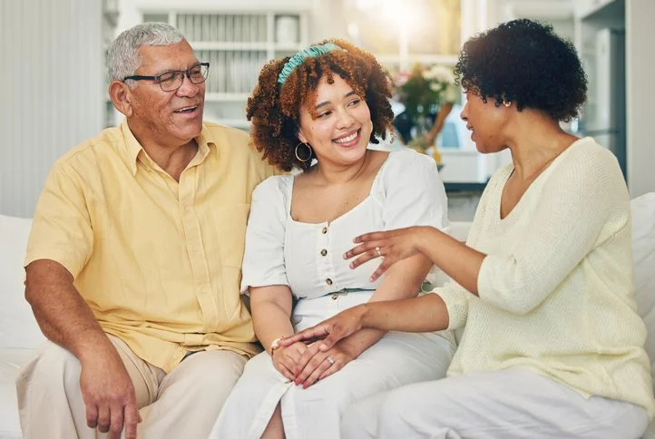 Adult child sitting with older parents on couch, smiling and having a conversation