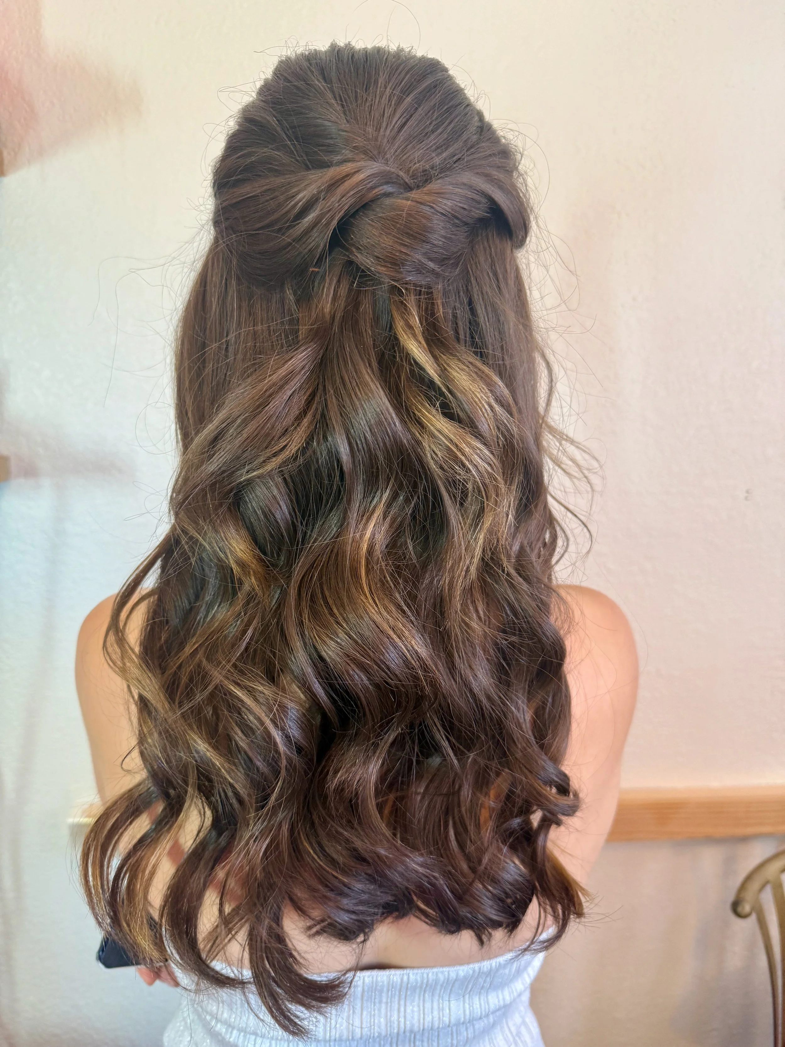 Bride with long, wavy brown hair styled in loose curls, viewed from the back in a neutral setting.