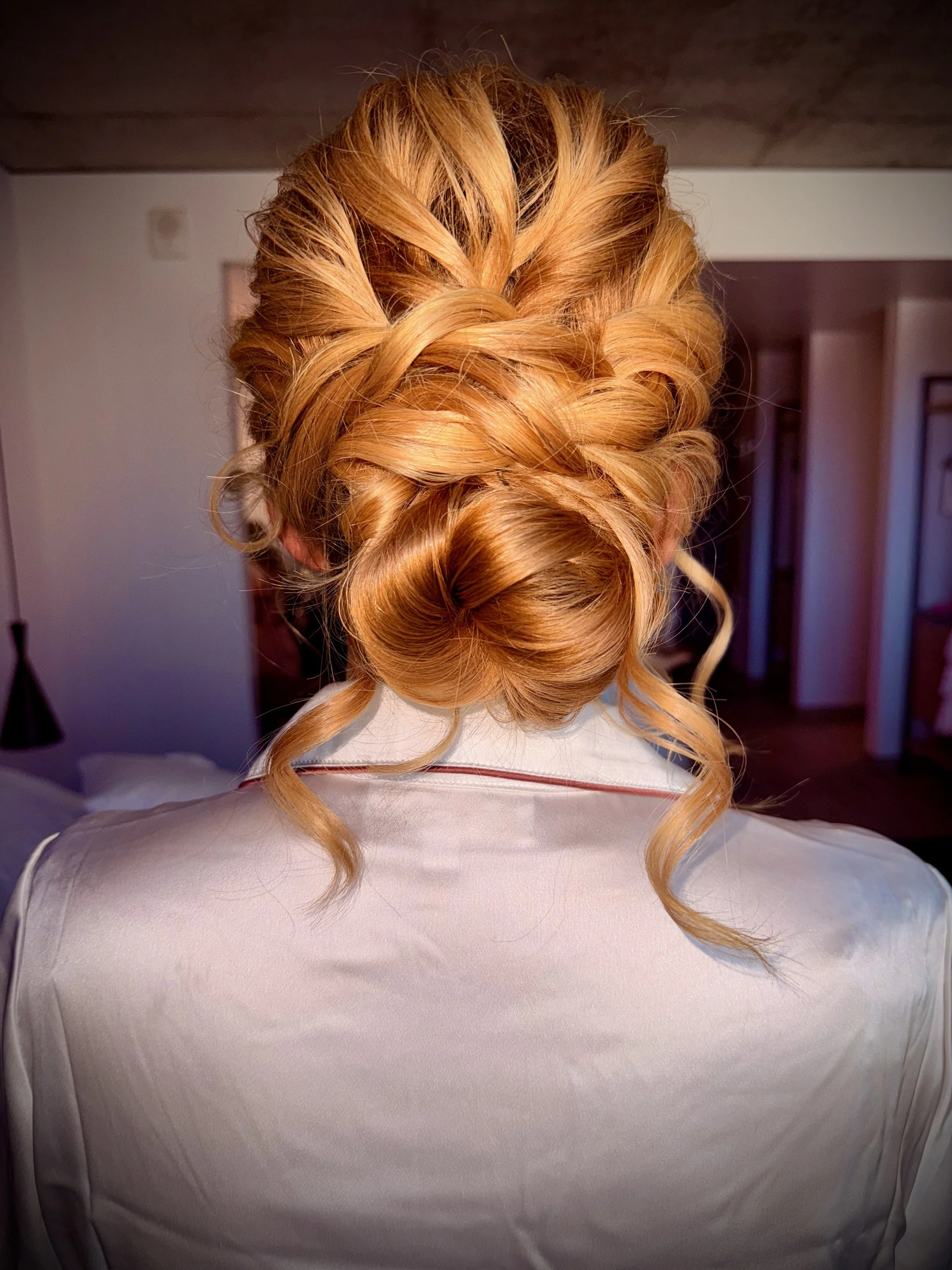 Bride with blonde hair styled in an elaborate updo,  with a white satin robe.