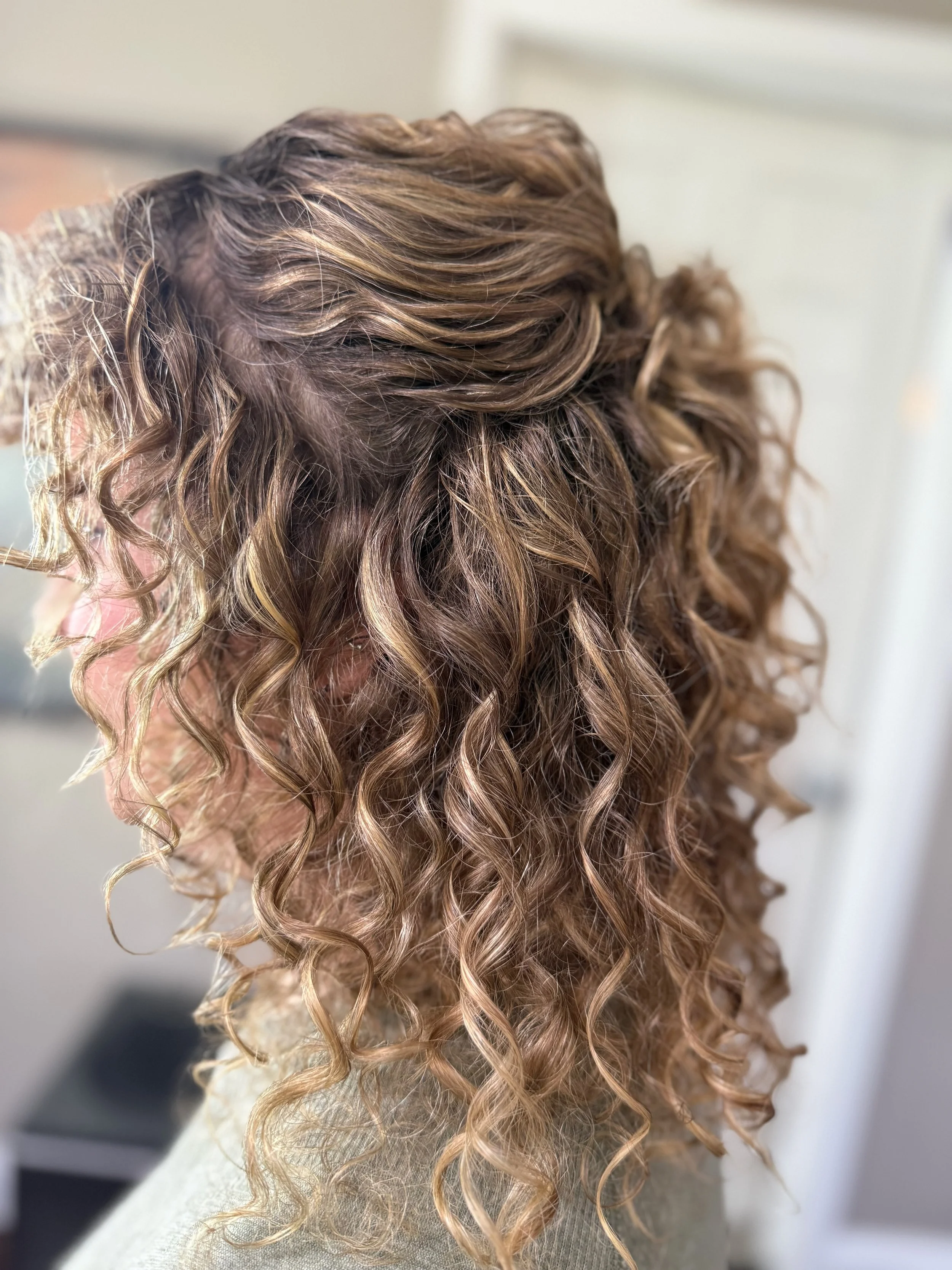 Close-up of curly, blonde hair with highlights, styled in loose ringlets.