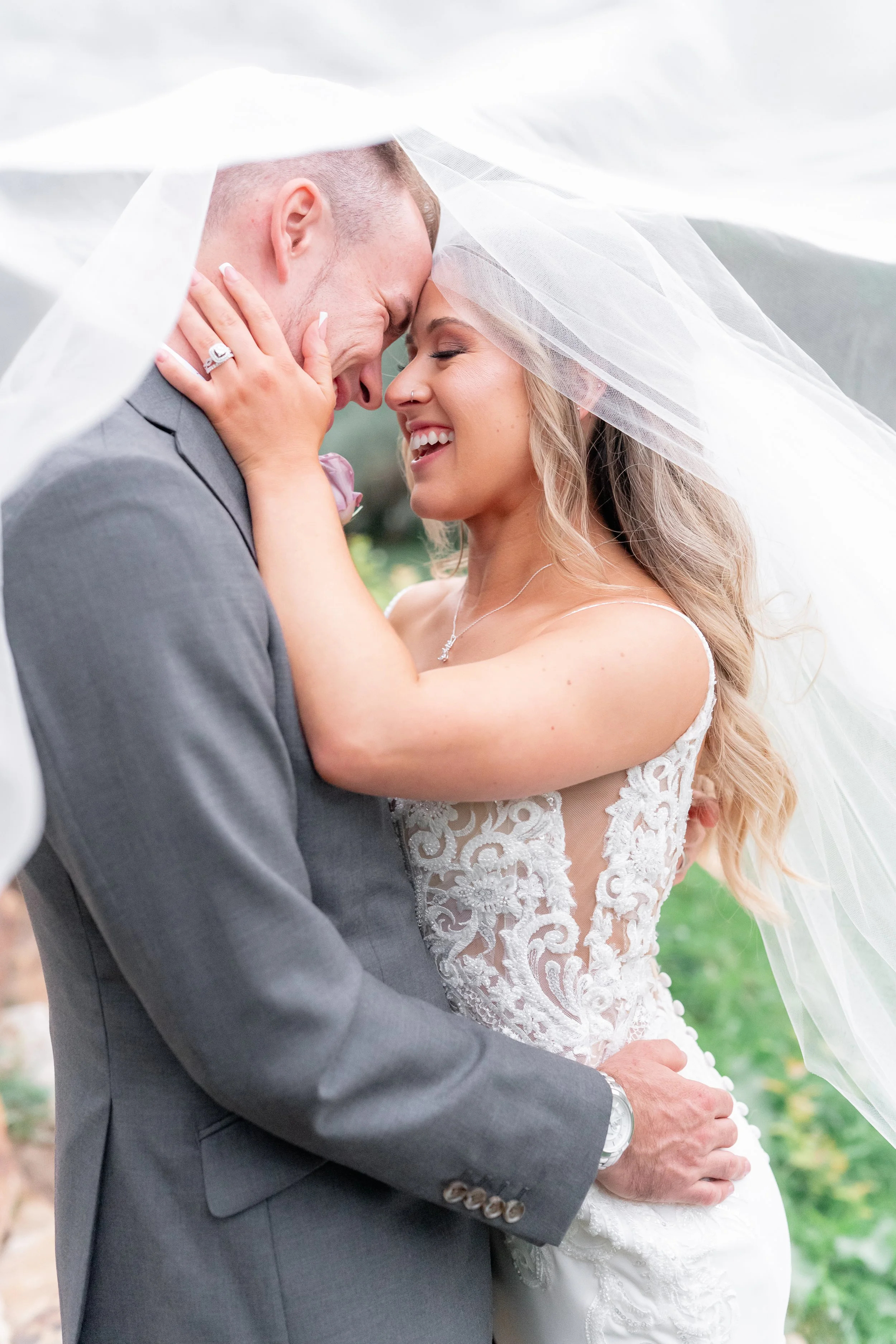A bride and groom sharing a joyful moment under a veil during their wedding celebration, dressed in wedding attire.
