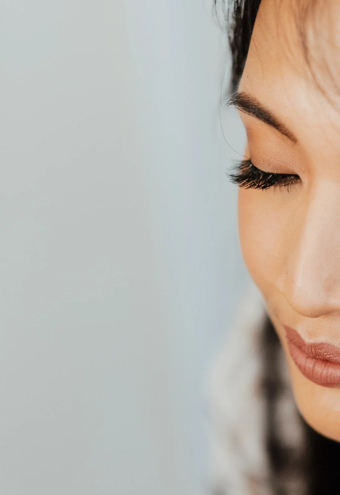 Close-up of an Asian woman's face with her eyes closed, showing her eyelashes, eyebrows, and part of her lips.