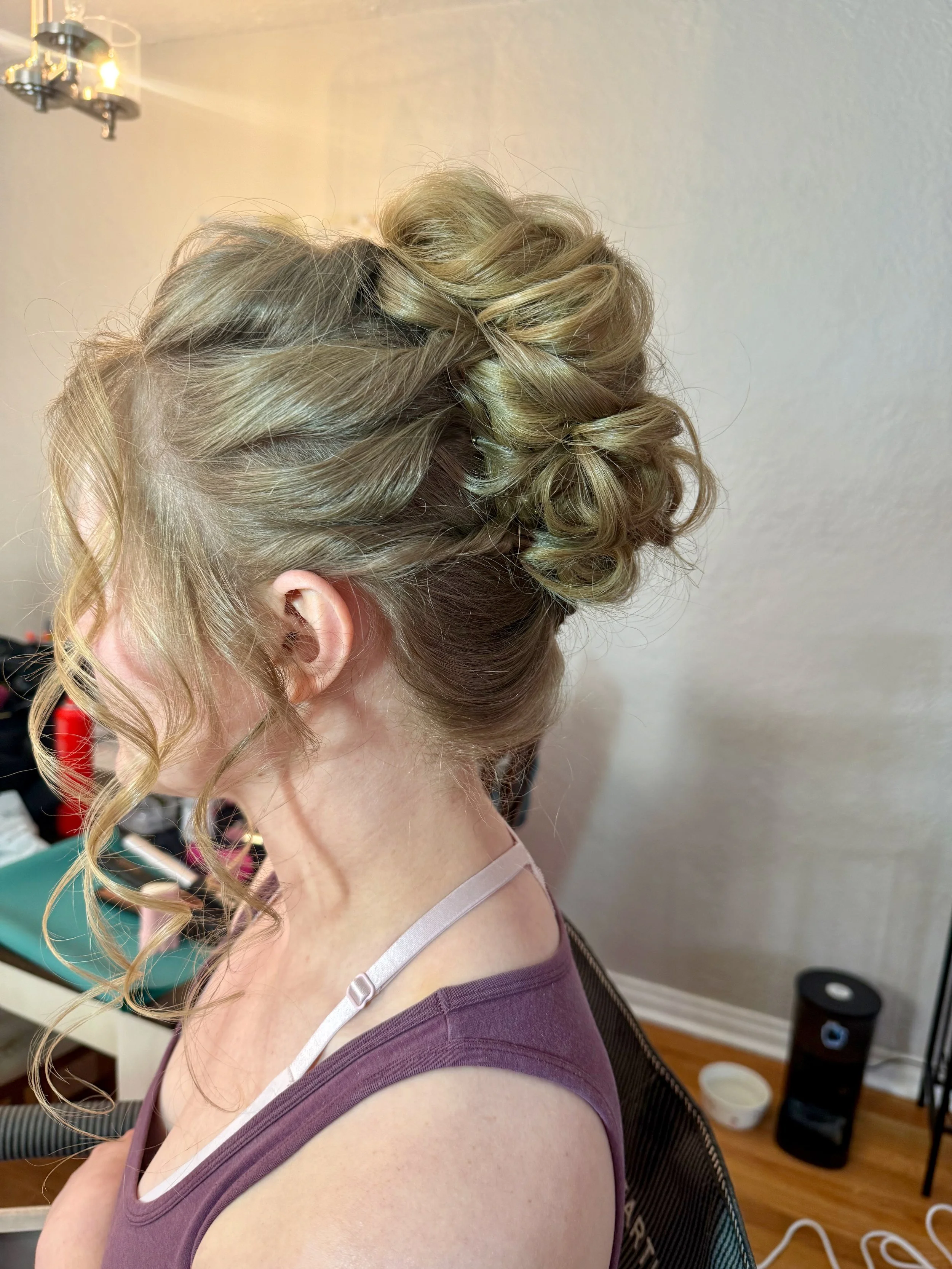 Bride with styled blonde curly hair sitting in a room with a chandelier in the background.