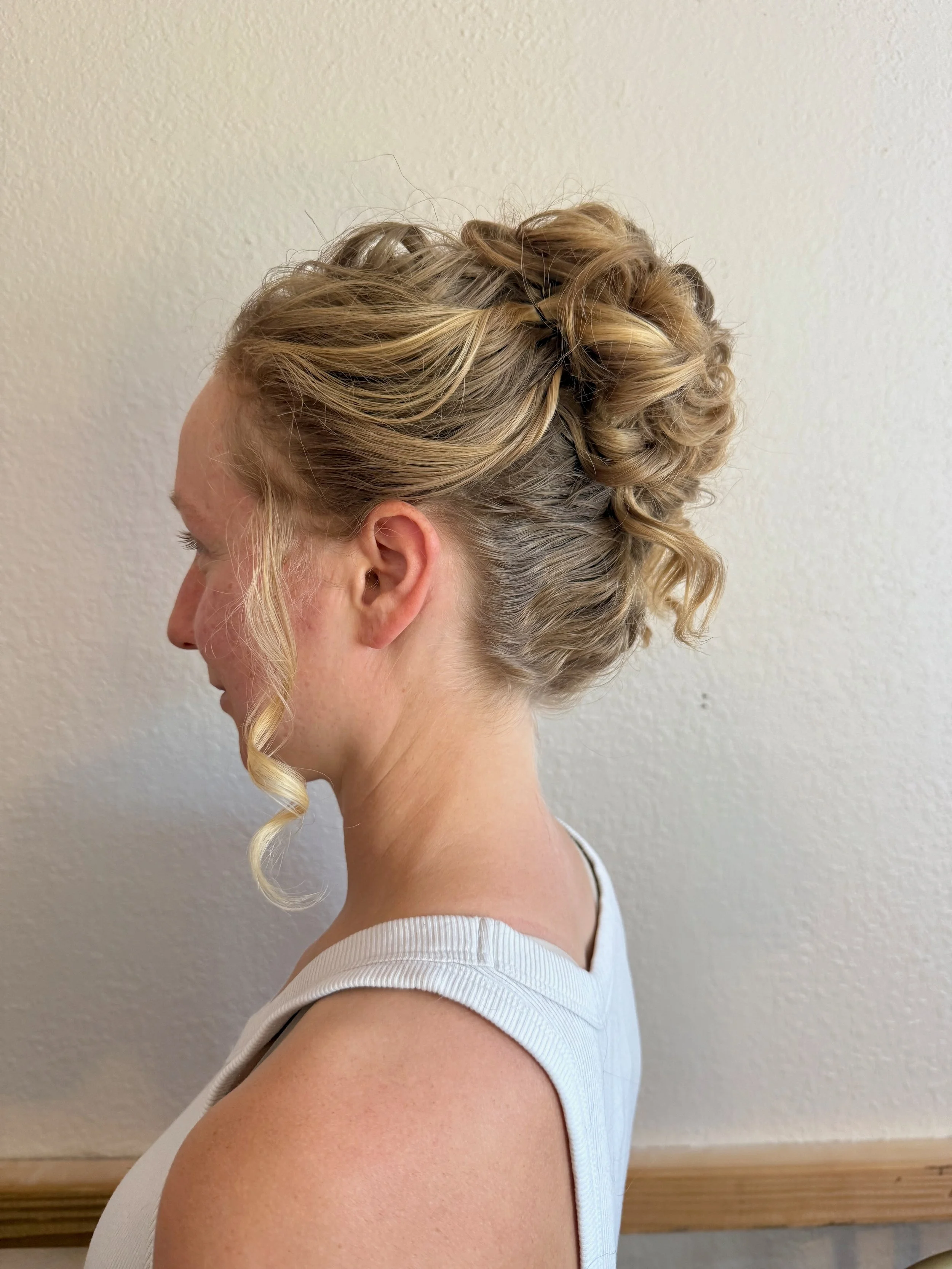 Side profile of a bride with an intricate updo hairstyle featuring twists and curls against a neutral background.