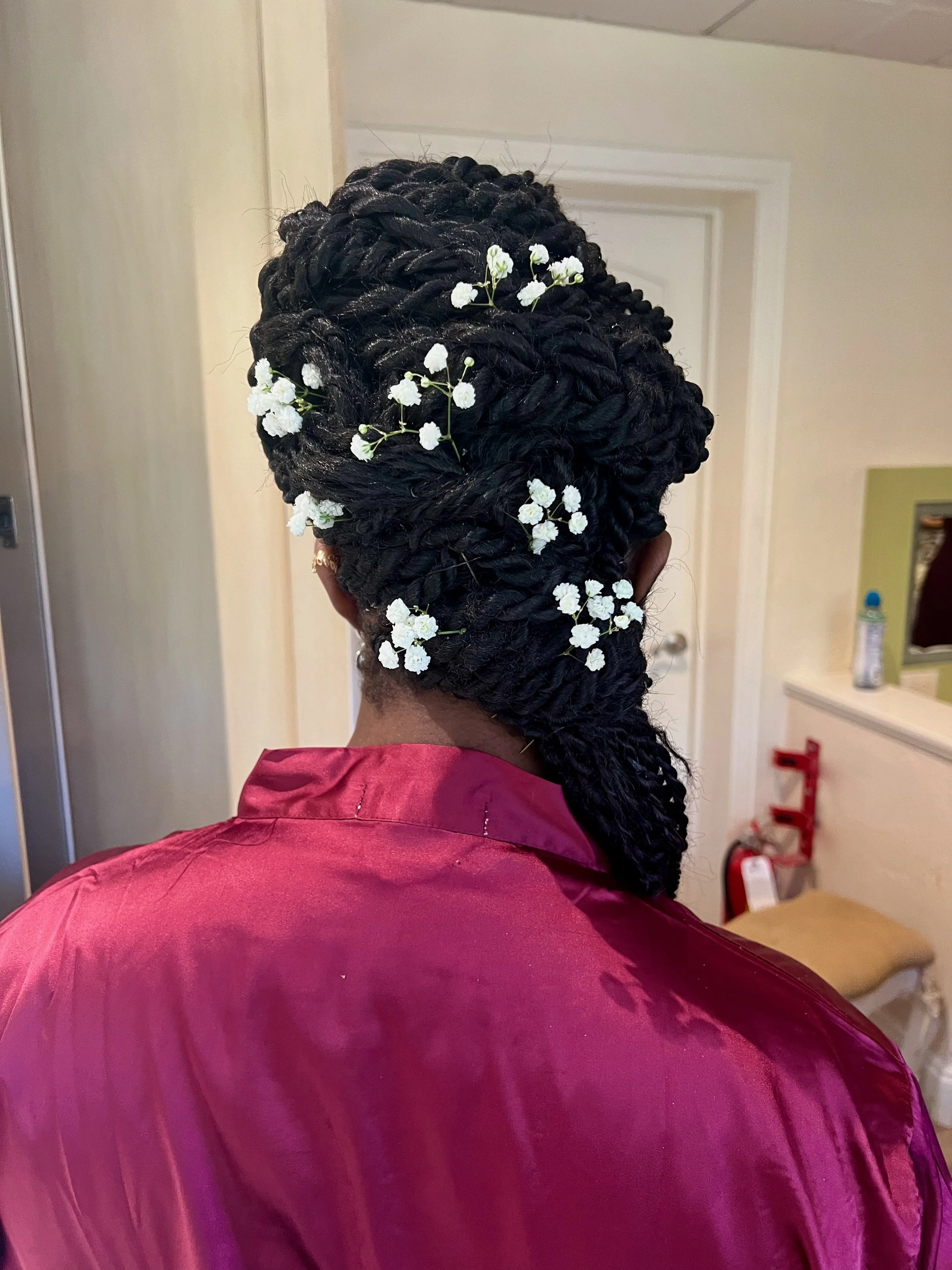 Back view of a bride with large, black, intricately styled braided hair adorned with small white flowers.