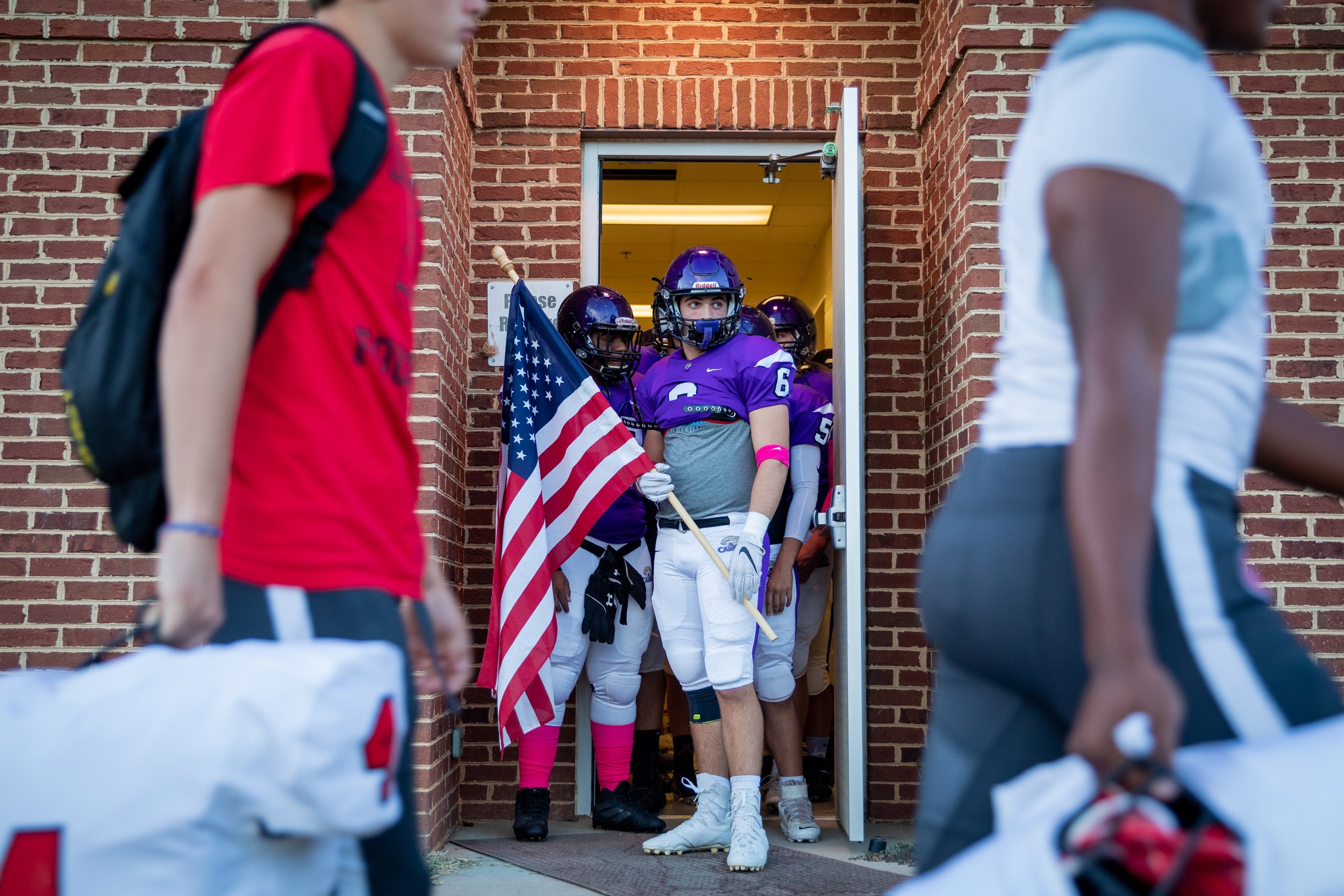  Senior, Braden Hunter holds the American Flag as he and his team get ready to storm the field, a tradition the team performs before every home game. Walking past the team are members of the opposing team, the Graham High School Red Devils. 