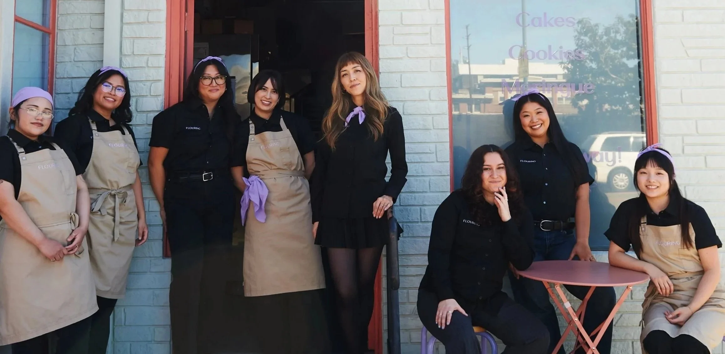 team photo of owner , bakers, and retail staff in front of bakery kitchen door.