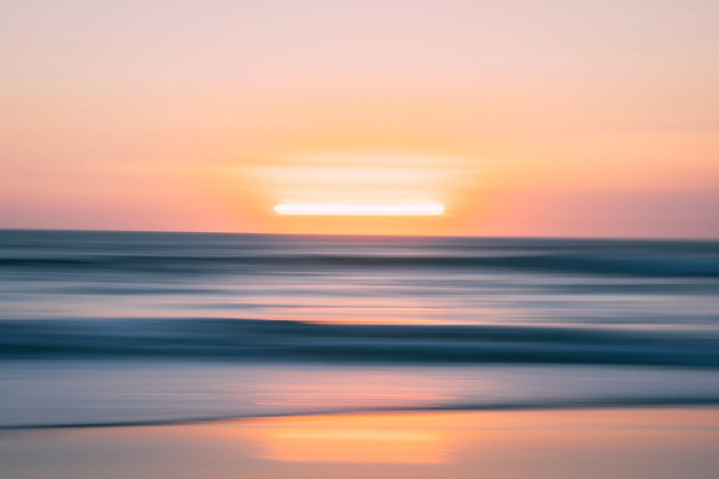 A blurred seascape at sunset with a warm orange glow on the horizon and soft pastel pink and purple sky.
