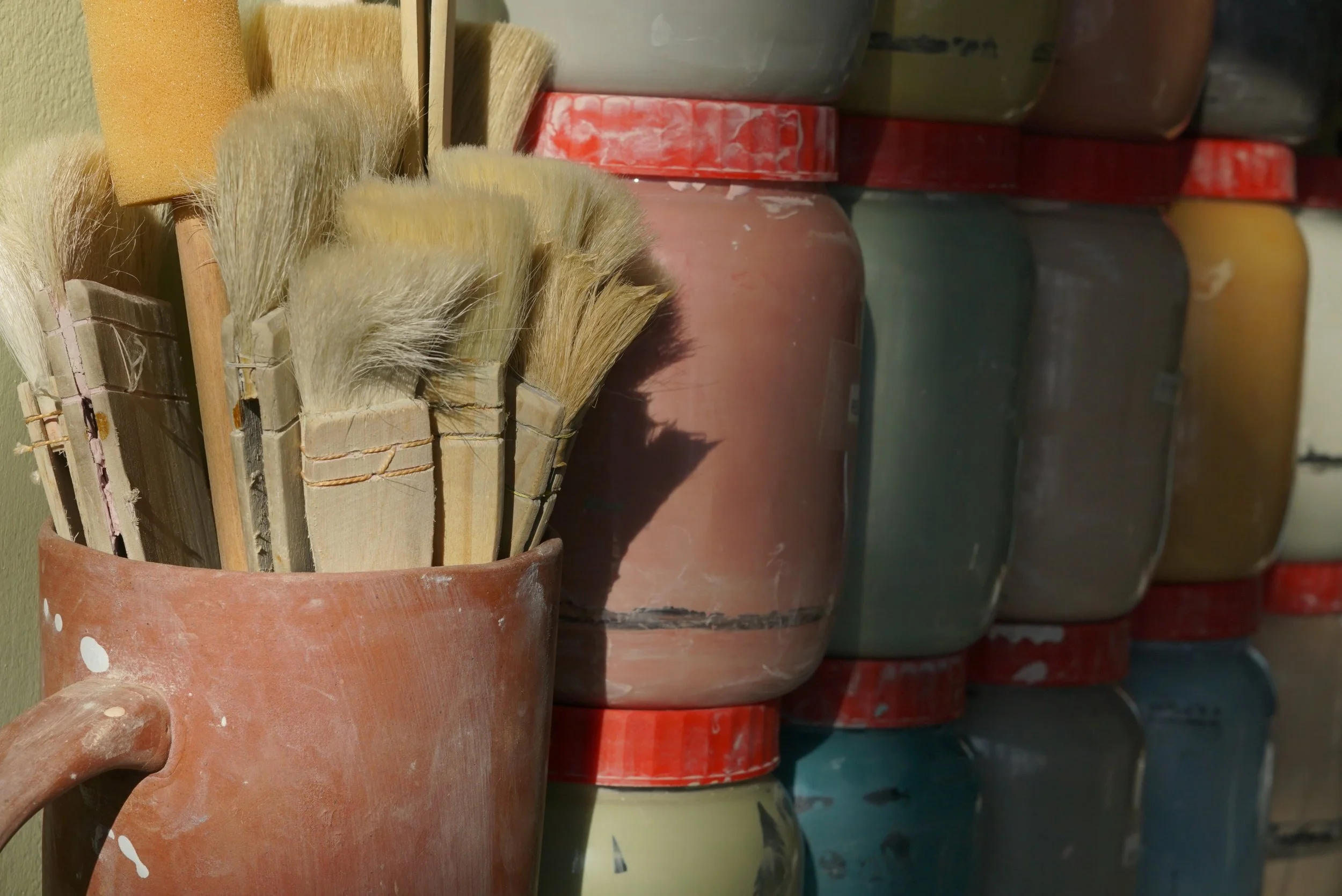 Natural warm light ceramic studio paint brushes and pots of coloured slip