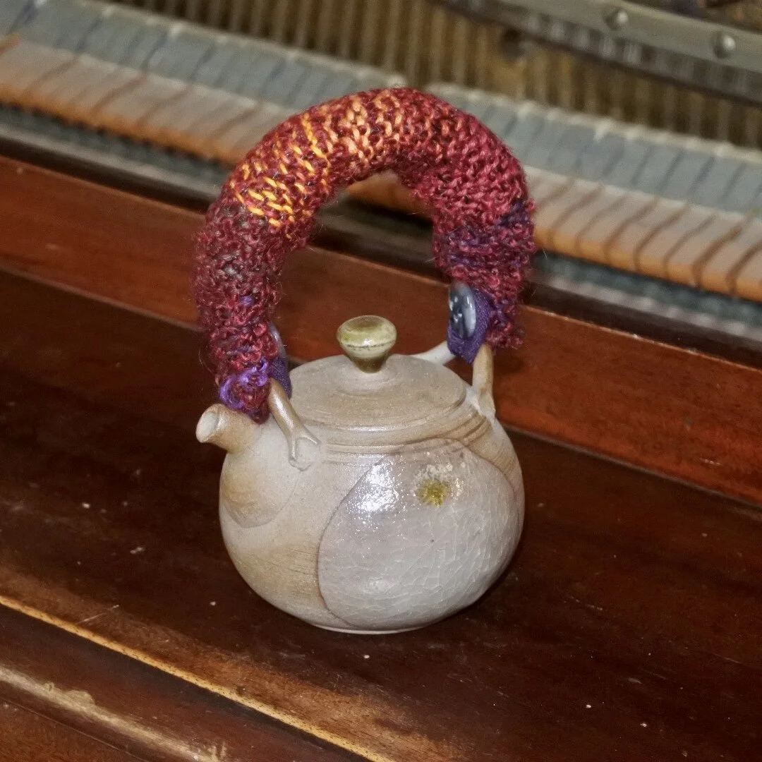 Teapot with a fabric handle sitting on top of an old piano.