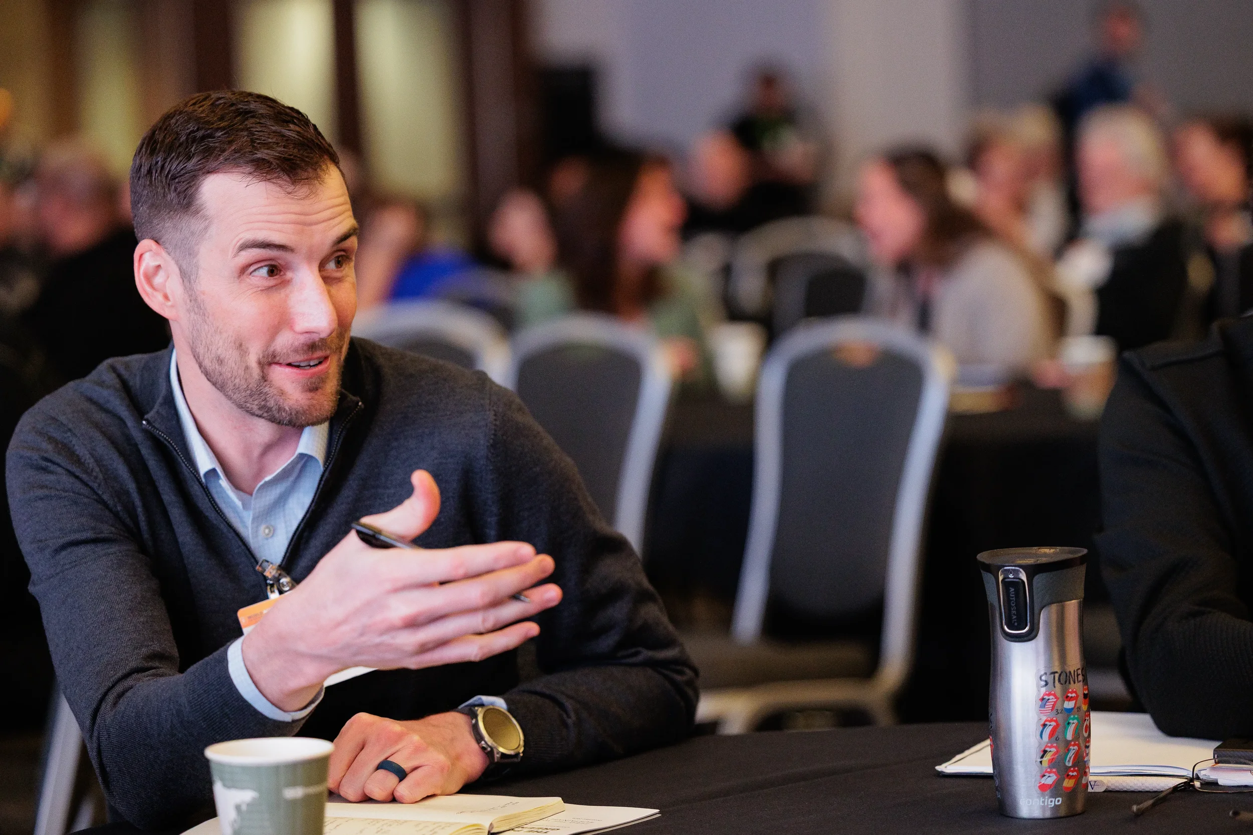 Badged attendee gestures expressively while speaking at table during Orlando corporate conference session