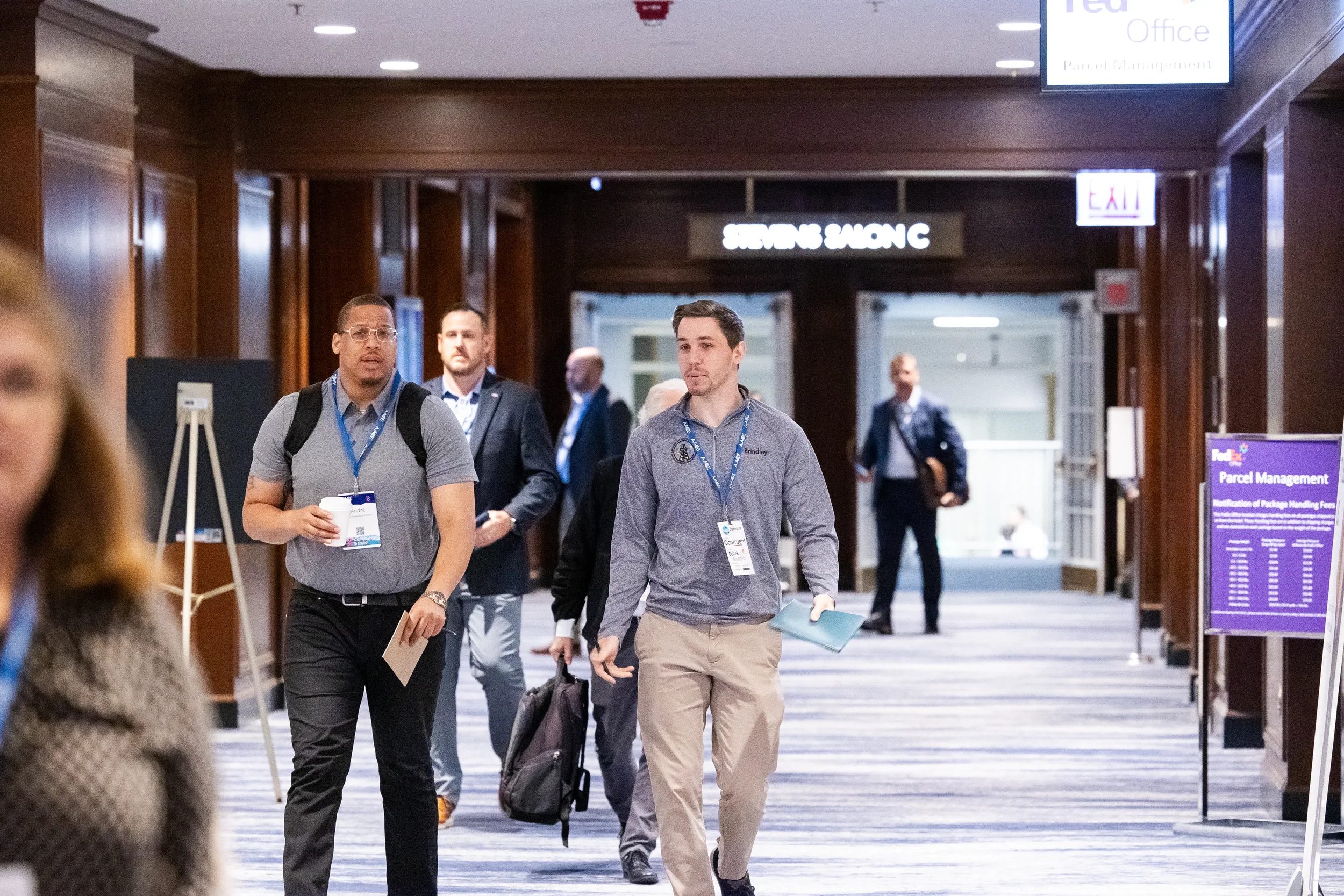 Attendees with lanyards walk through a wood-paneled hallway between sessions at a Chicago industry conference