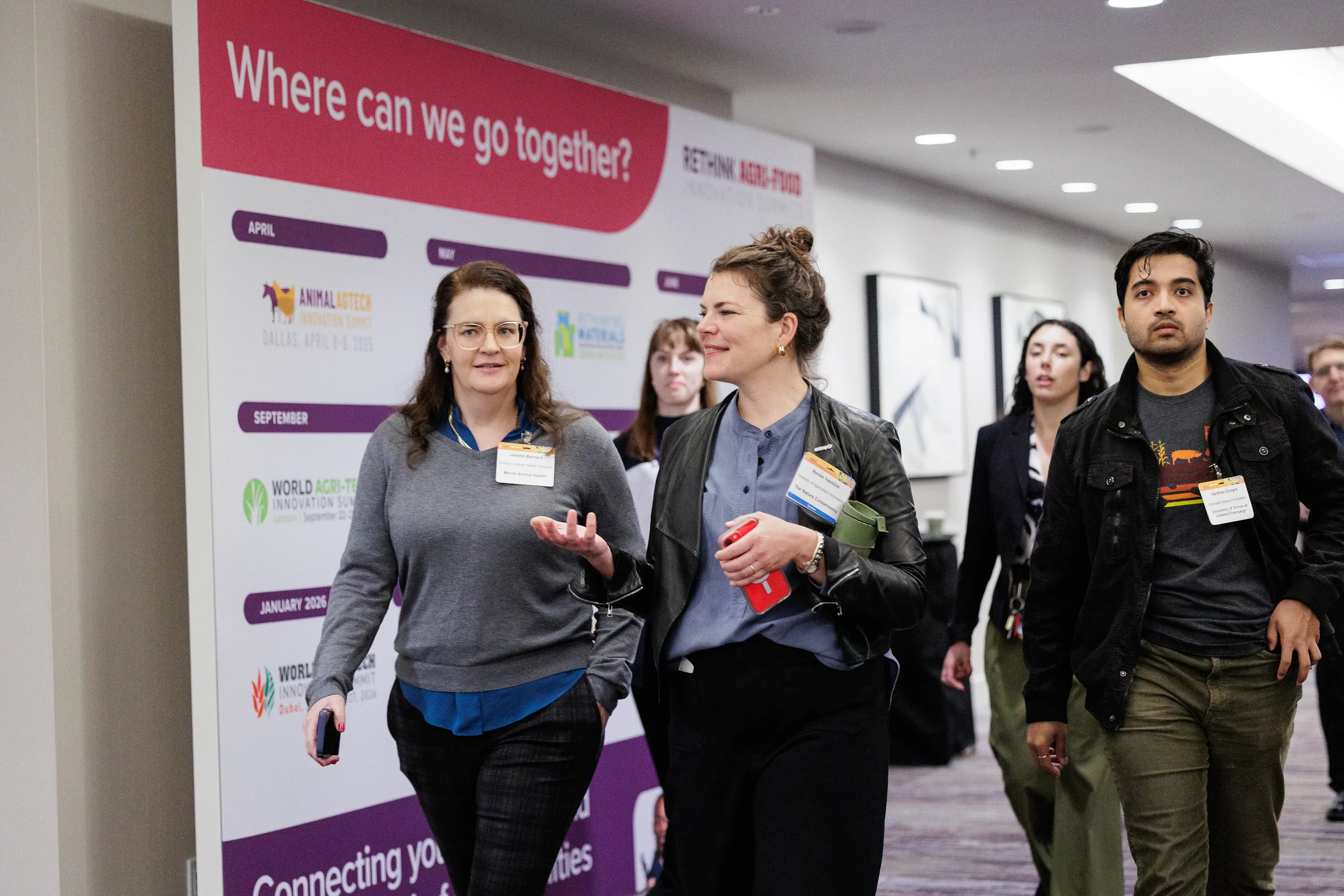 Attendees with name badges walk and converse past branded signage in Orlando corporate conference hallway