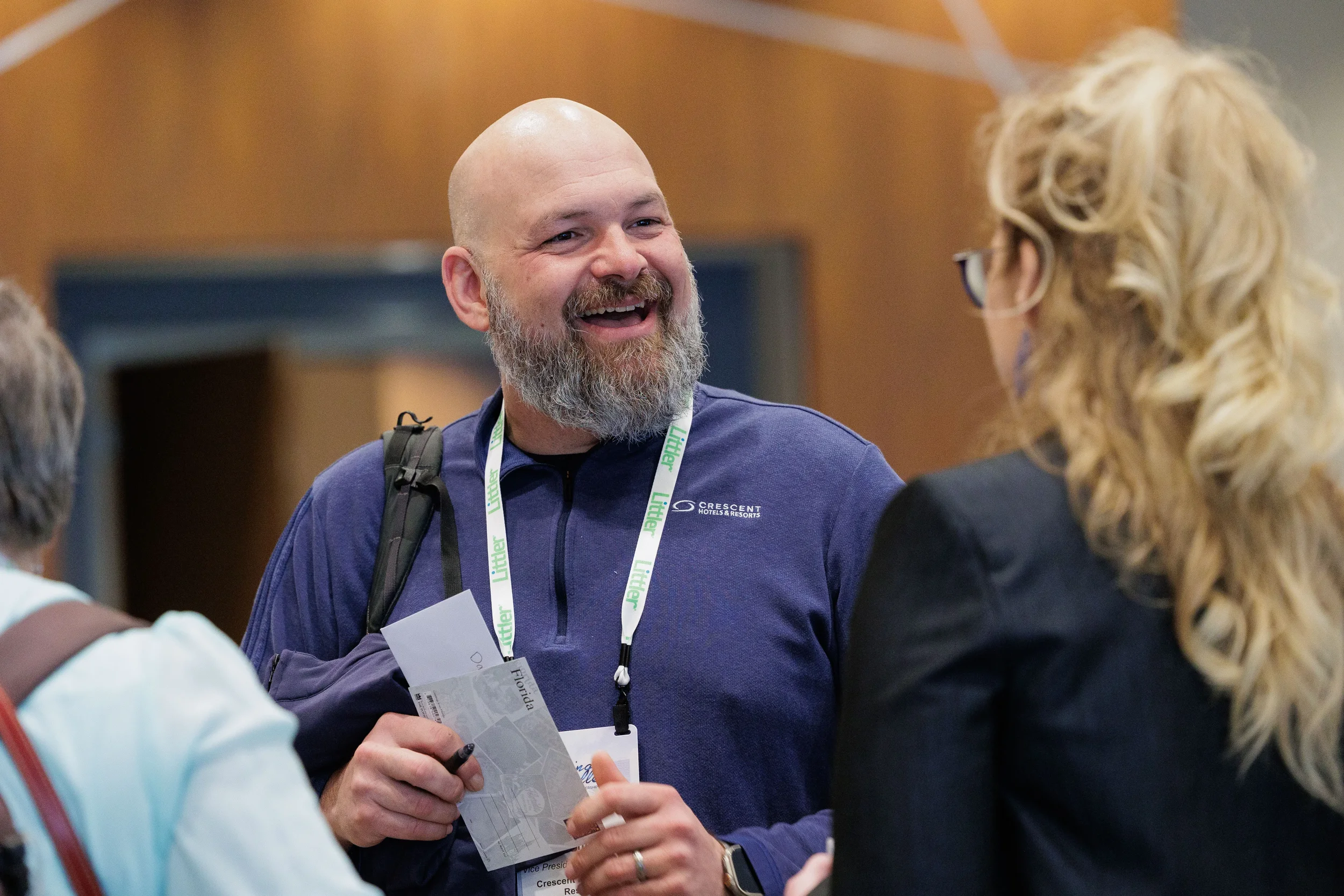 Smiling male attendee with lanyard holds materials while conversing at Orlando industry conference