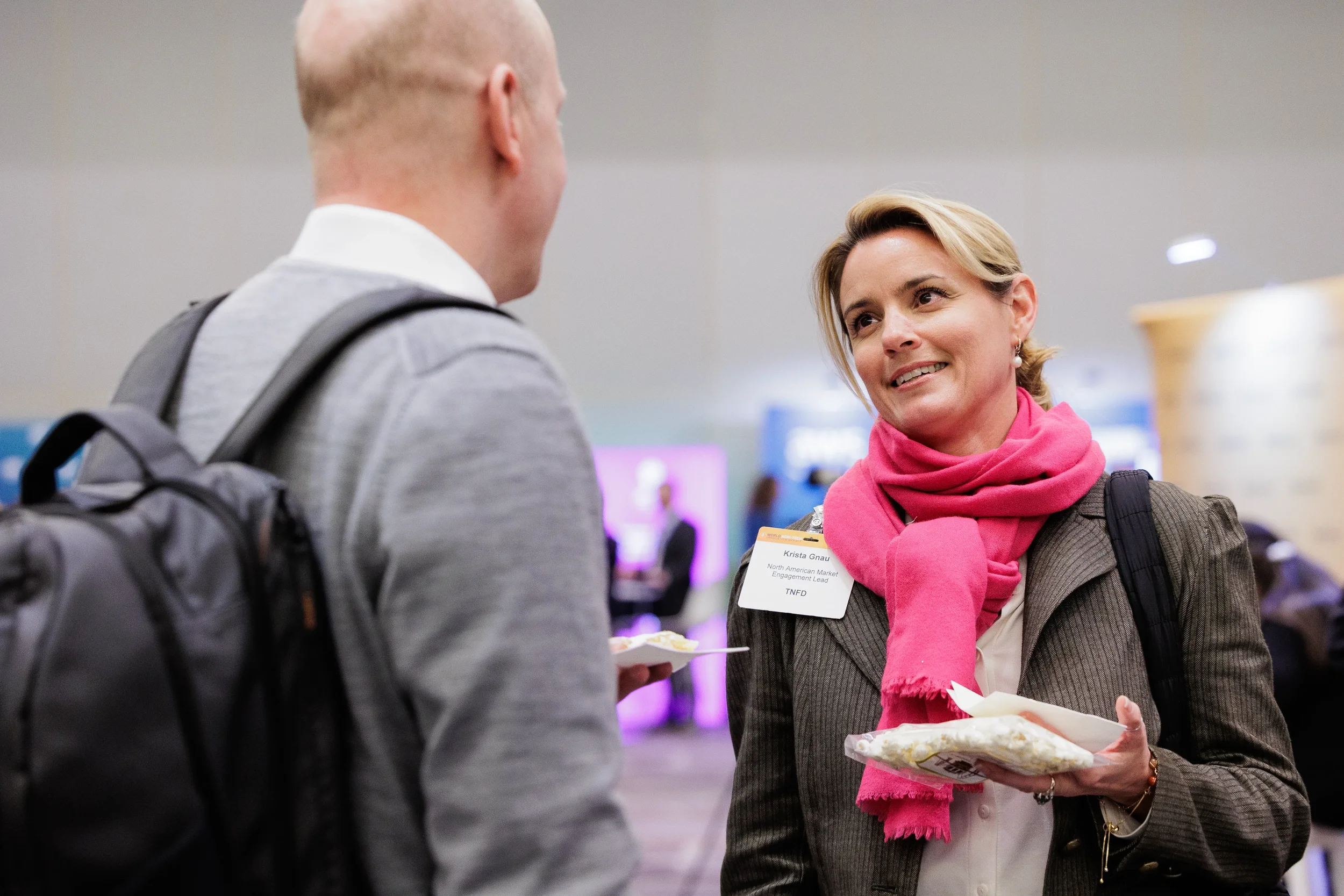 Badged attendee in pink scarf chats with another while holding snacks at Chicago corporate conference