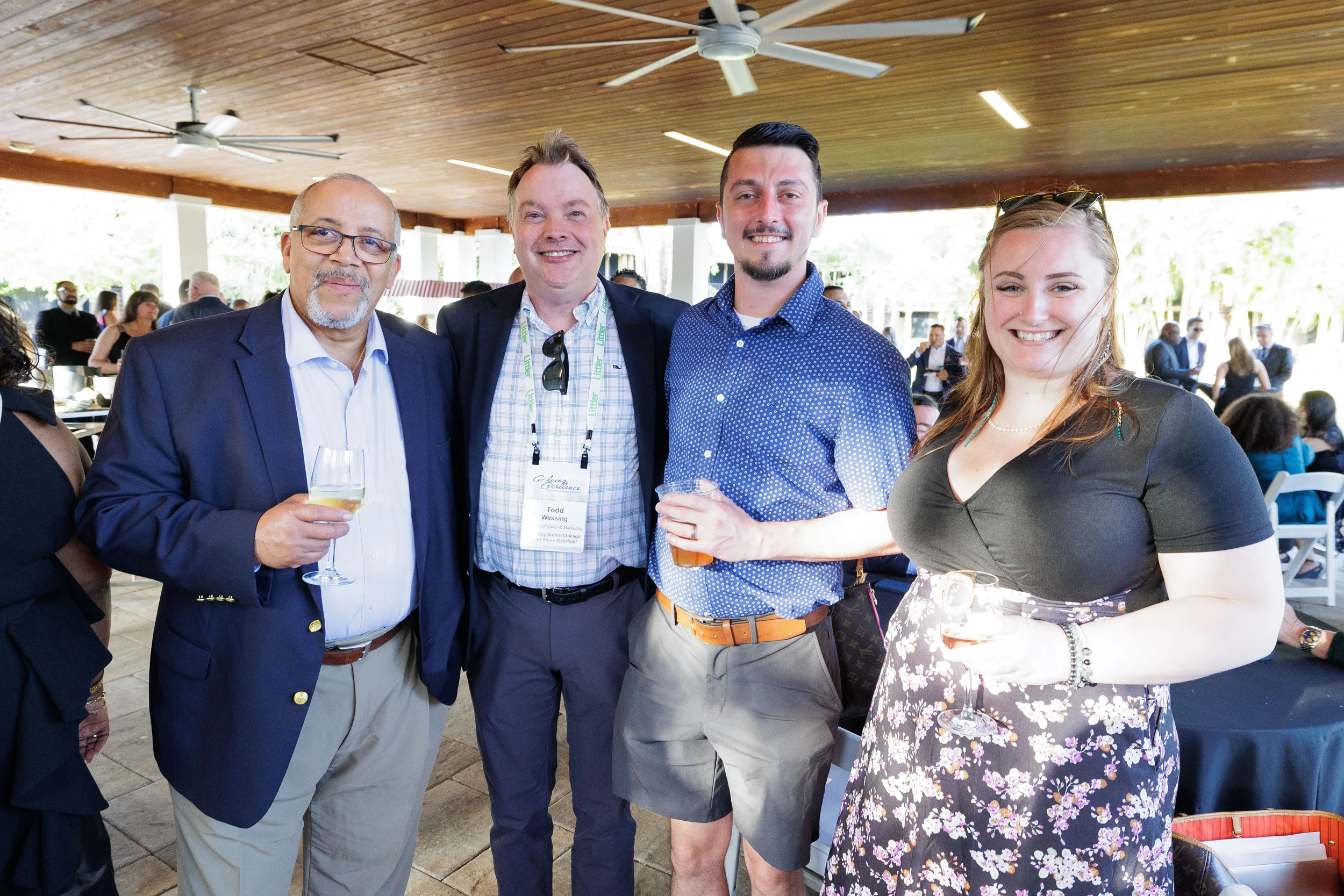 Four attendees with lanyards pose and smile with drinks at outdoor pavilion at Orlando corporate event
