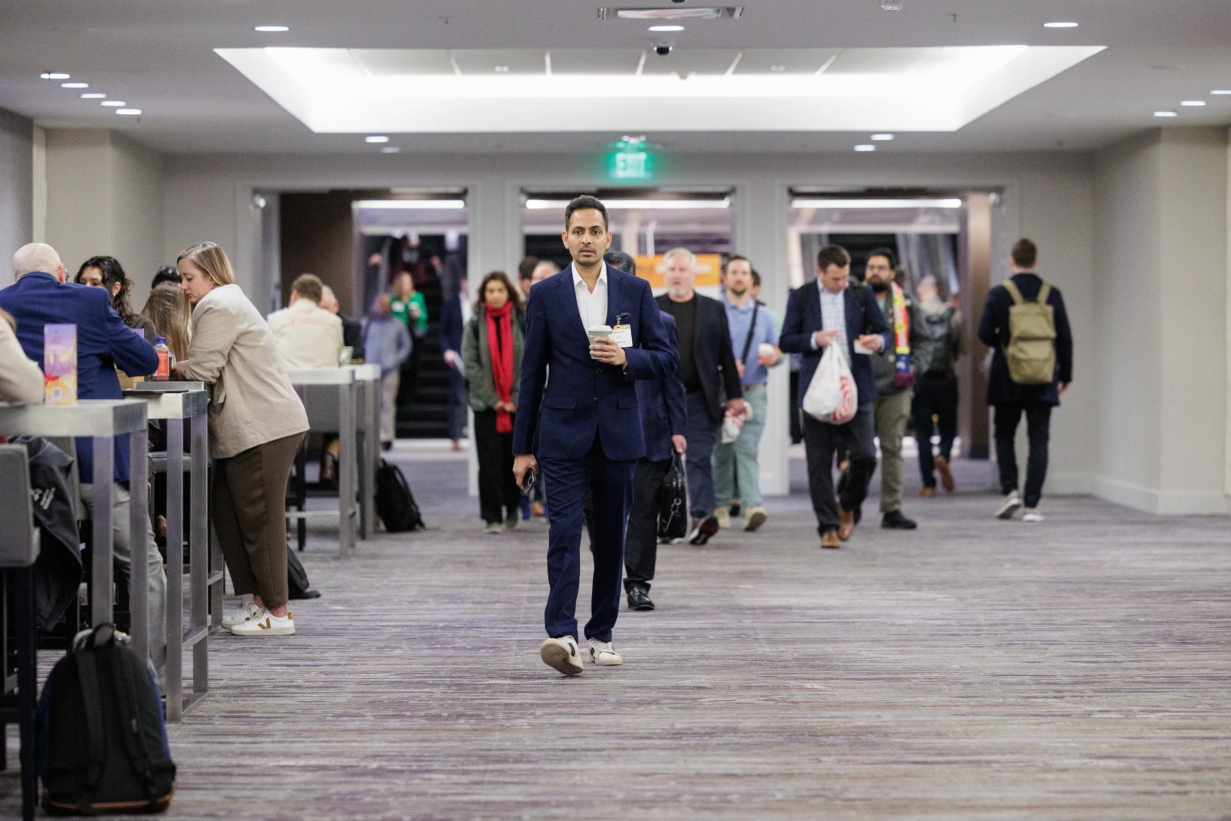 Attendee in navy suit walks through corridor holding coffee at Chicago industry conference