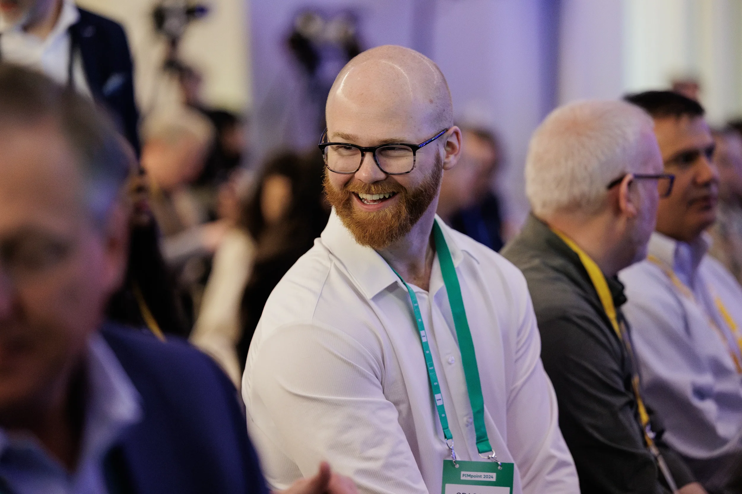 Smiling attendee with green lanyard glances over shoulder in seated audience at Orlando industry conference