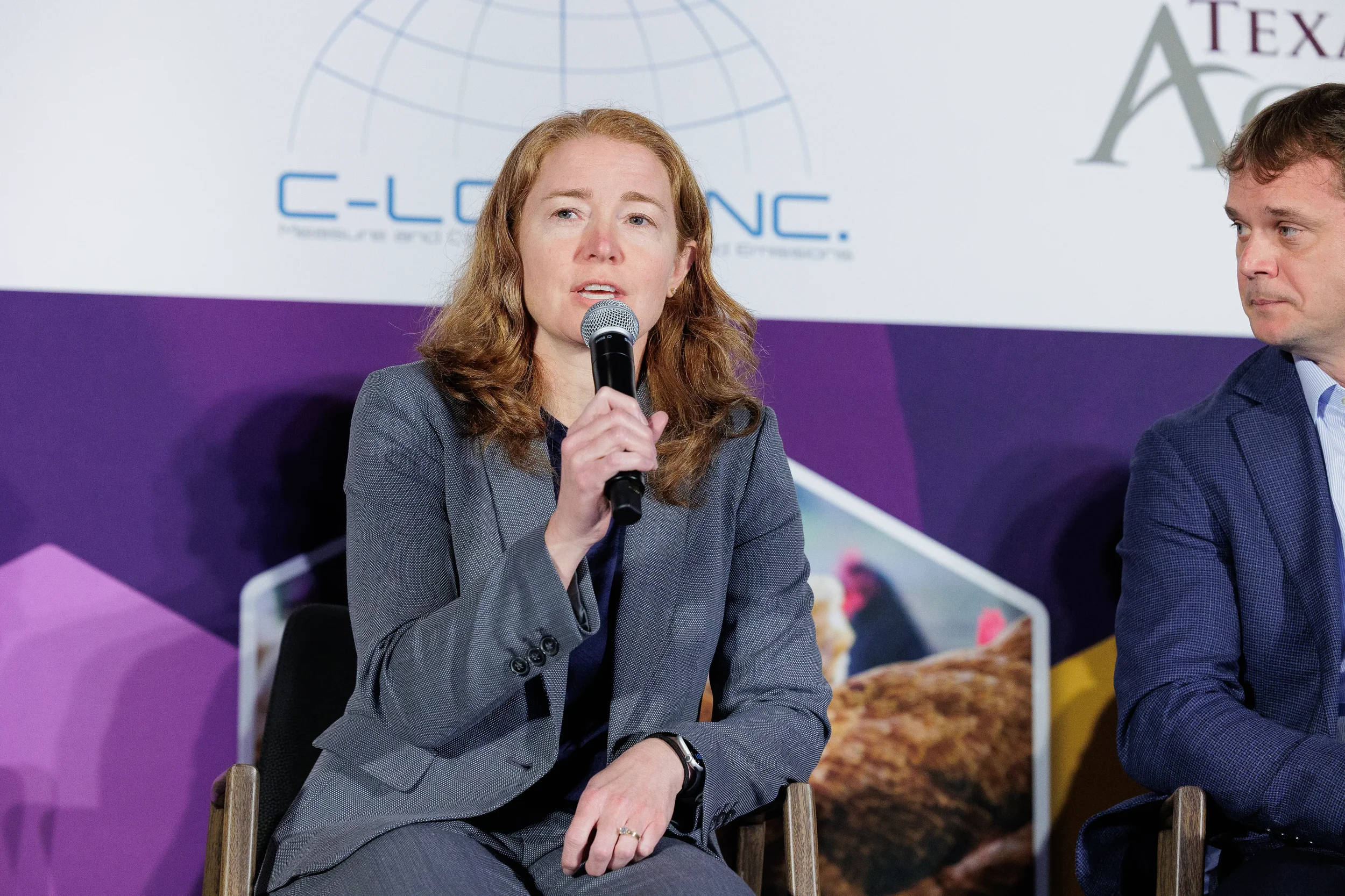 Speaker holds microphone while addressing panel at branded stage at Orlando industry summit