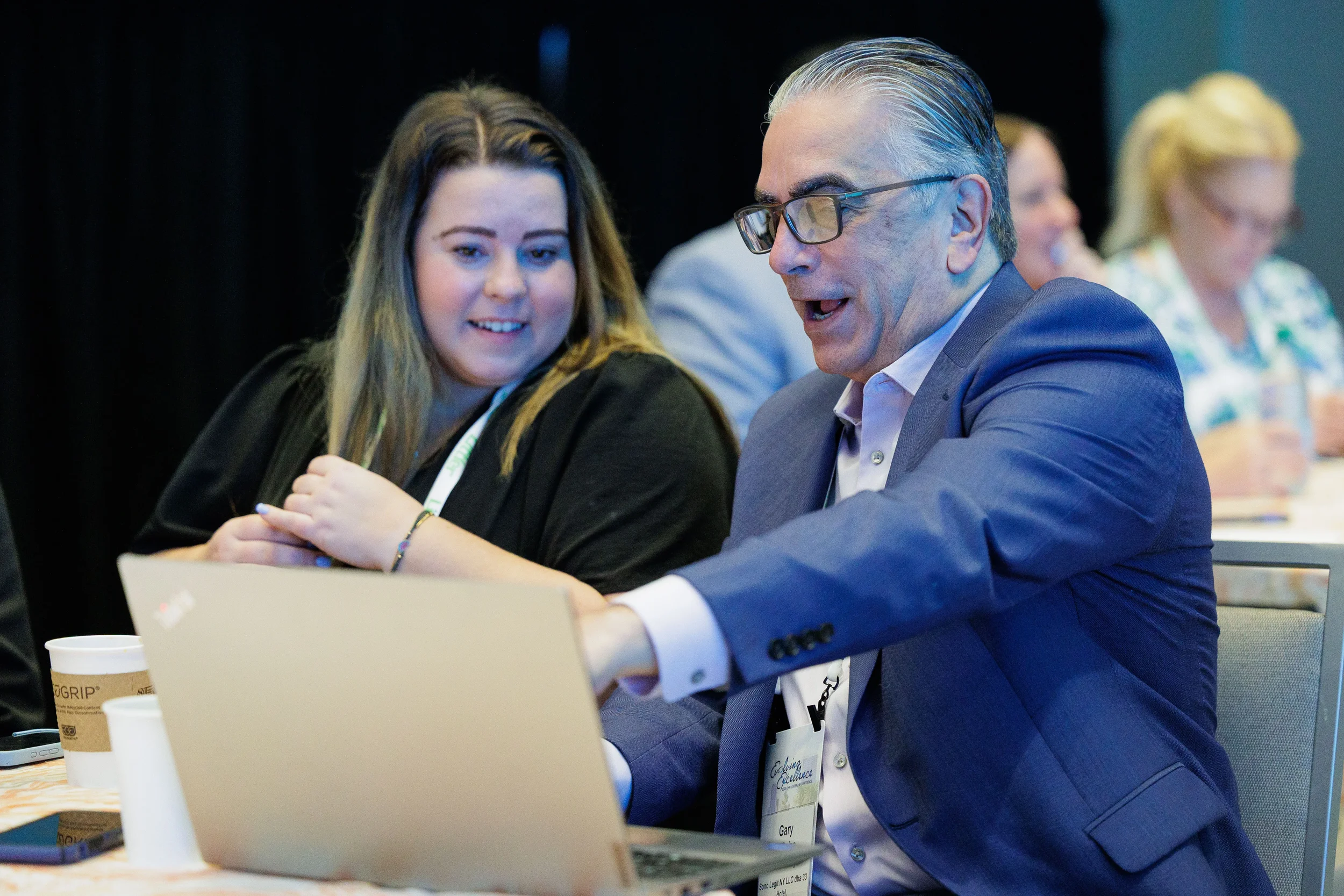 Two attendees with lanyards review laptop together during seated session at Orlando industry conference