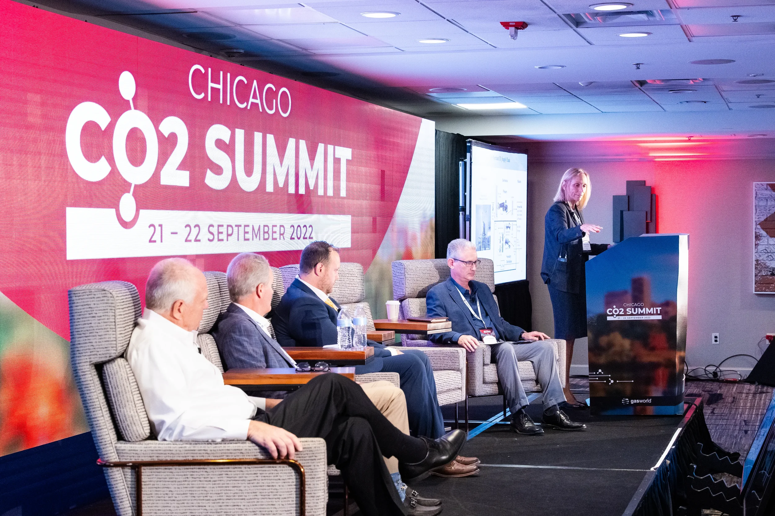 Presenter speaks from podium while panelists listen on stage at Chicago industry conference