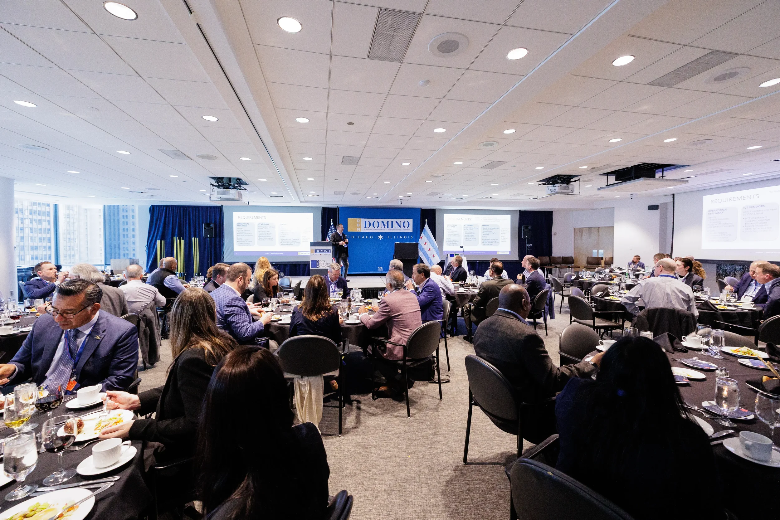 Speaker at branded podium addresses full room of attendees at round tables during Chicago corporate conference luncheon