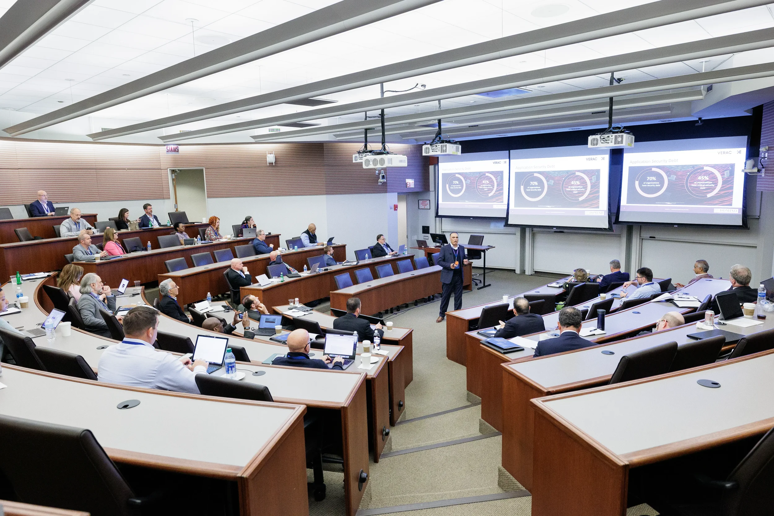 Speaker presents to tiered room of attendees in front of triple projection screens at Chicago corporate event