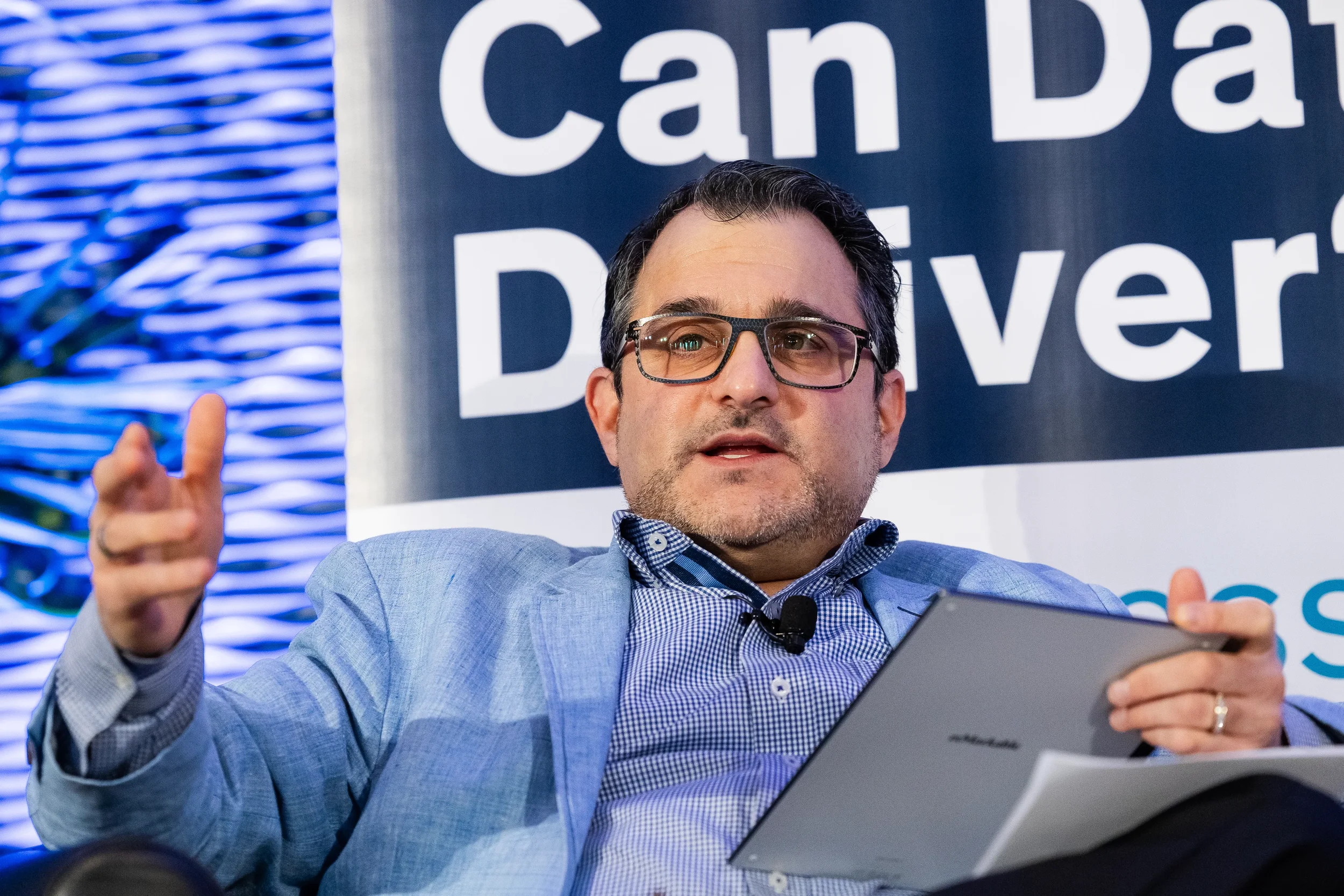 Panelist gestures while holding tablet during stage discussion at Orlando industry conference