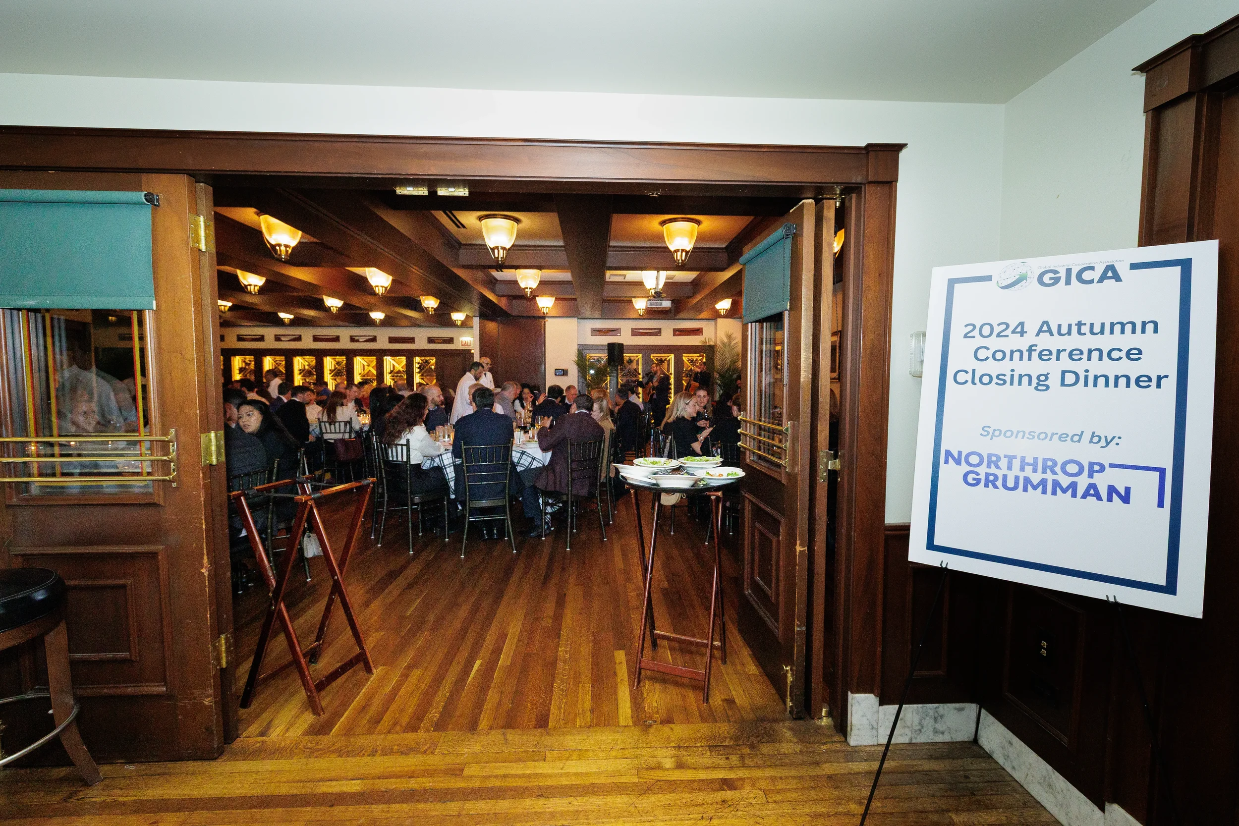 View through a dark wood doorway into a warmly lit room where people are seated for the Conference Closing Dinner in Chicago.