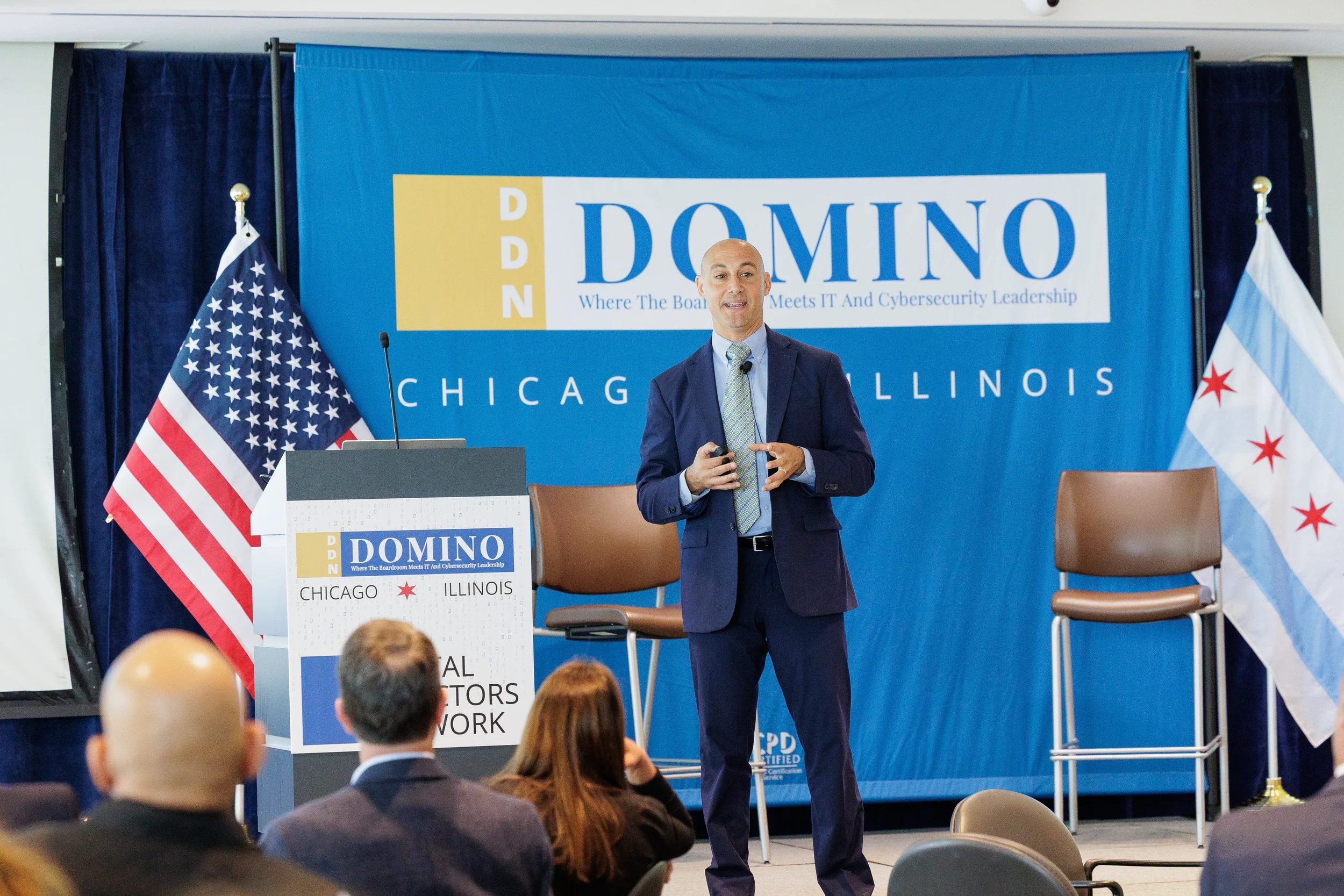 Male speaker gestures in front of branded stage backdrop with flags at Chicago corporate event