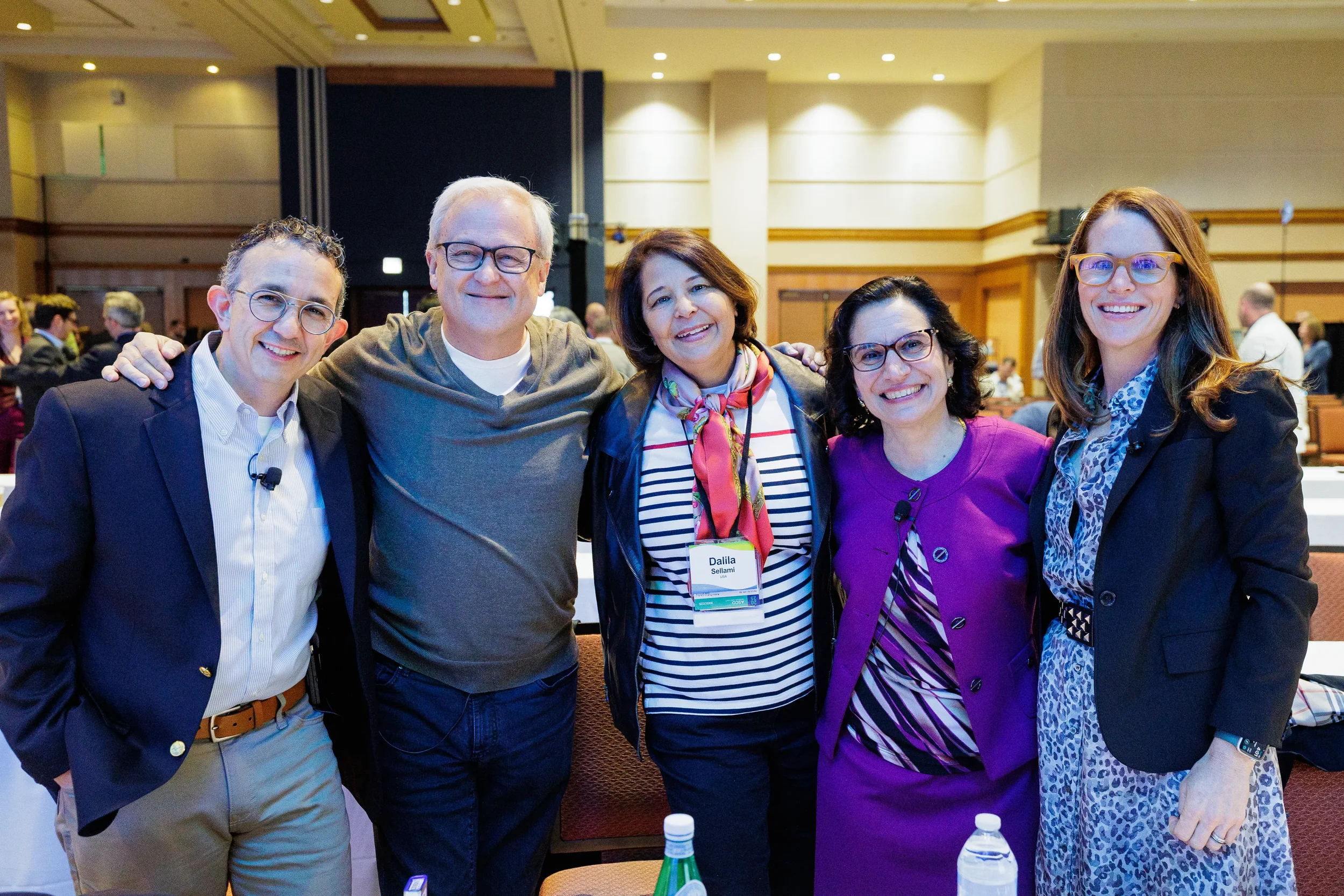Five smiling speakers pose with arms around each other in ballroom at Orlando industry conference