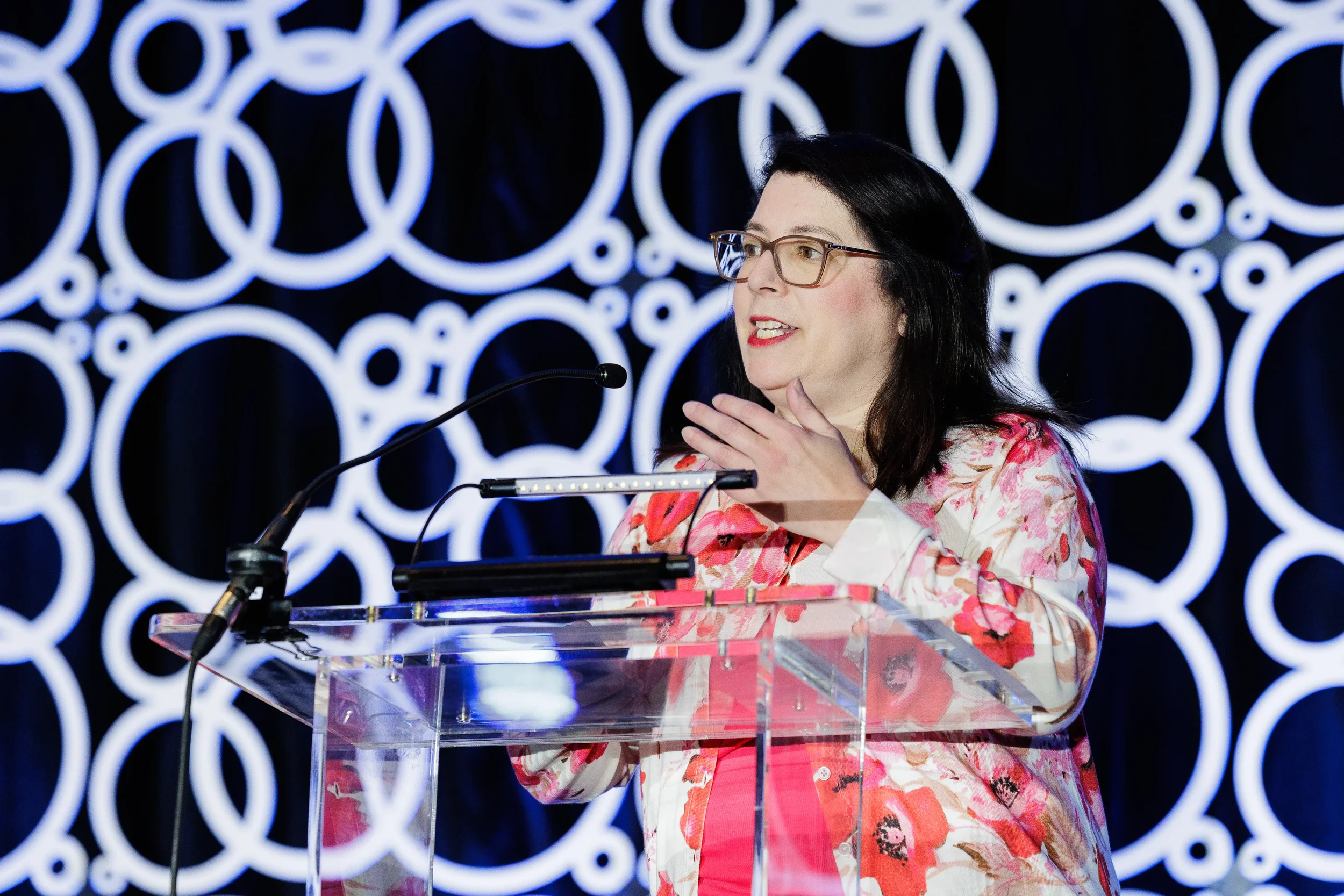Speaker presents from podium with illuminated circular backdrop at Orlando industry conference