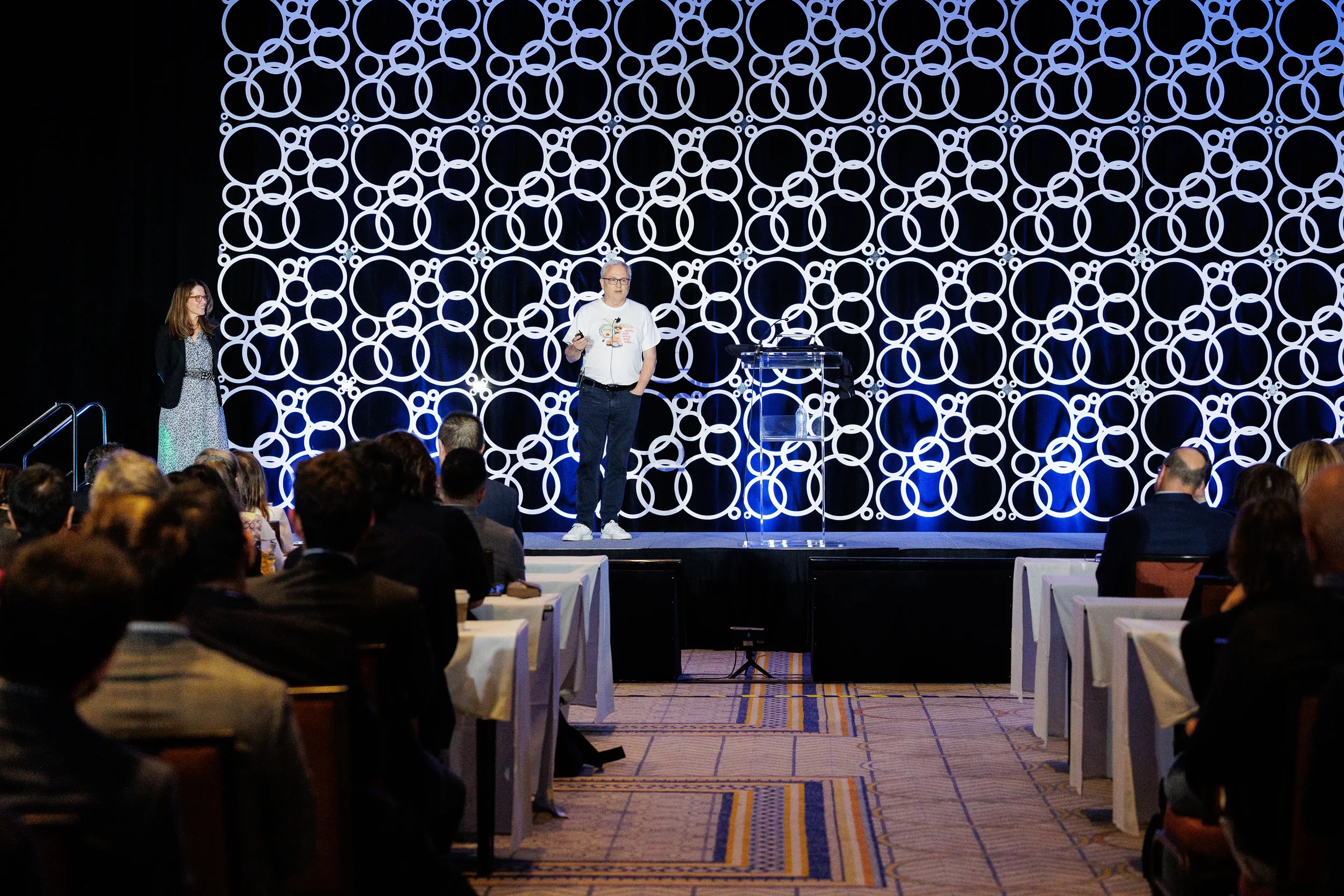 Speaker addresses audience on stage with illuminated circular backdrop at Chicago corporate event