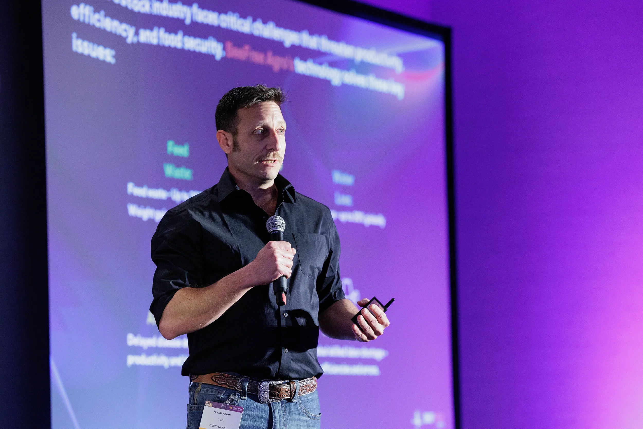 Speaker presents slide from stage while holding microphone at Orlando industry conference