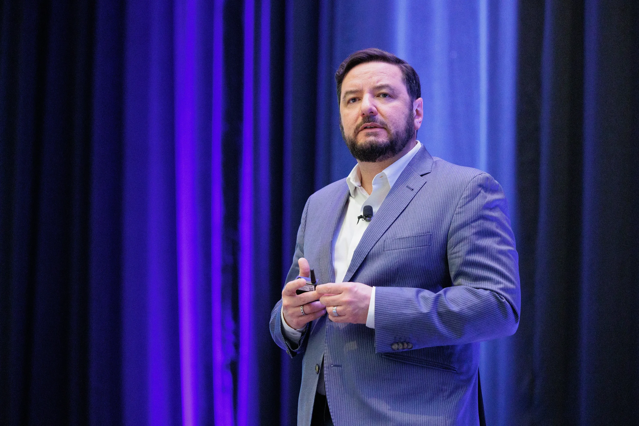 Bearded man in a blue suit jacket and white shirt presents on stage against deep purple curtains in Chicago.