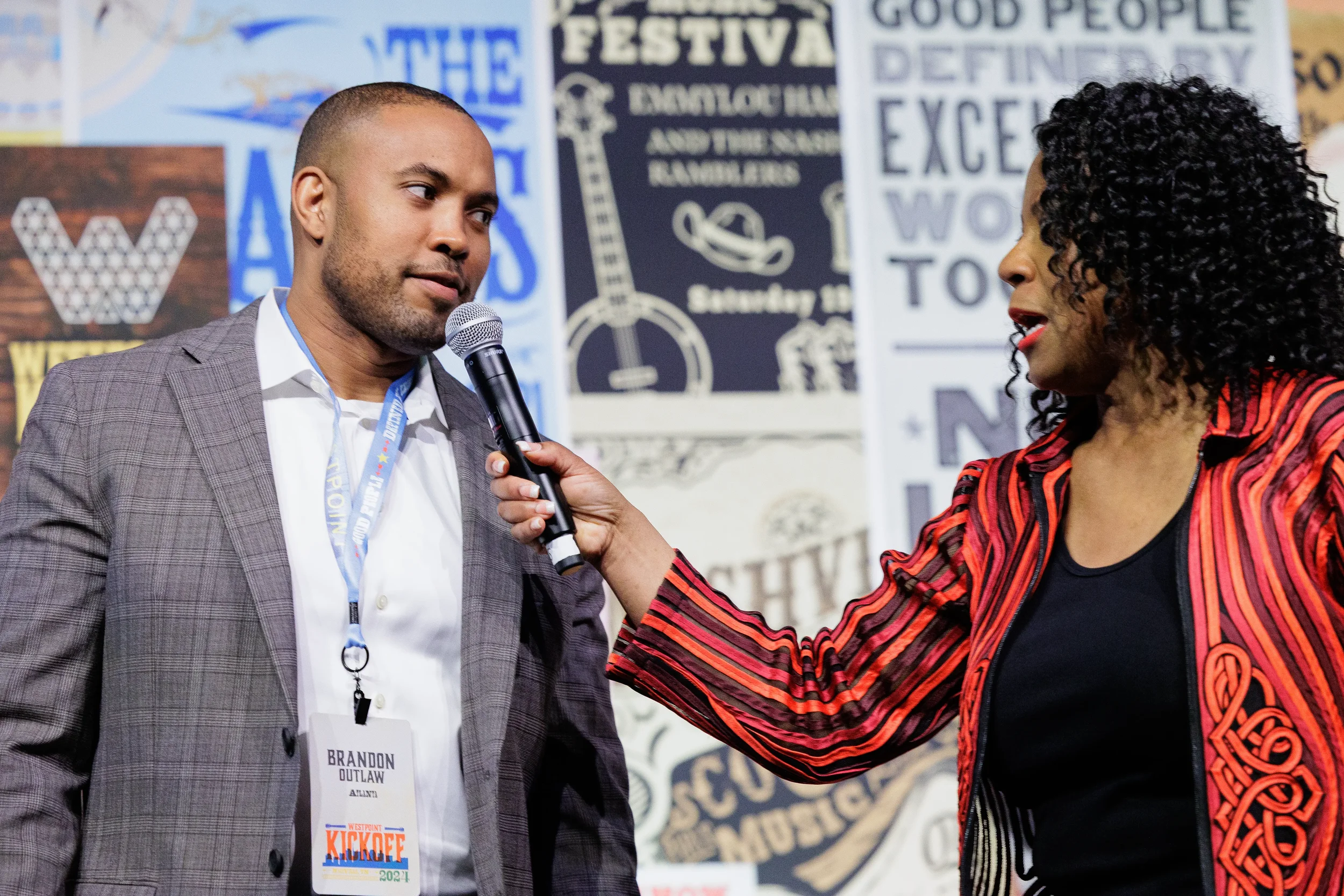 Host extends microphone toward attendee during on-stage interview in front of branded backdrop at Chicago corporate conference