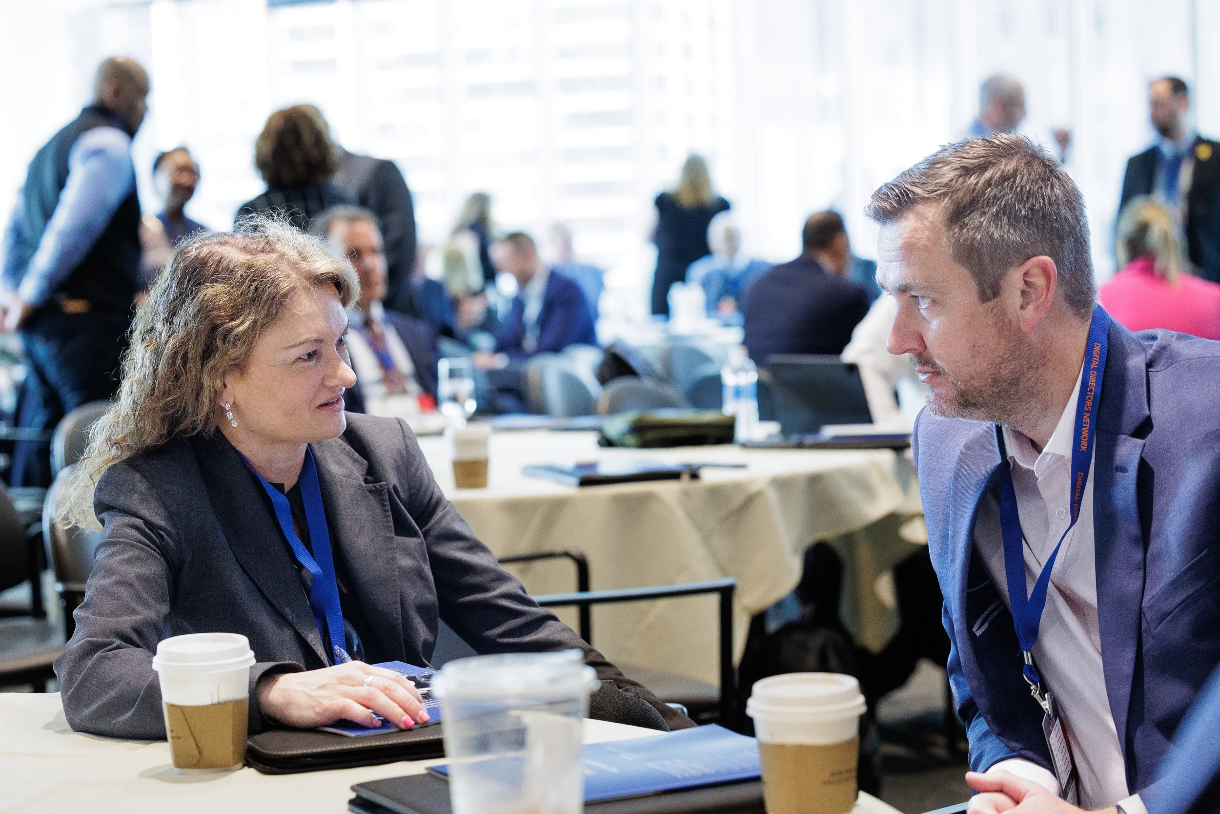 Two attendees with lanyards converse over coffee at table during Chicago corporate conference networking