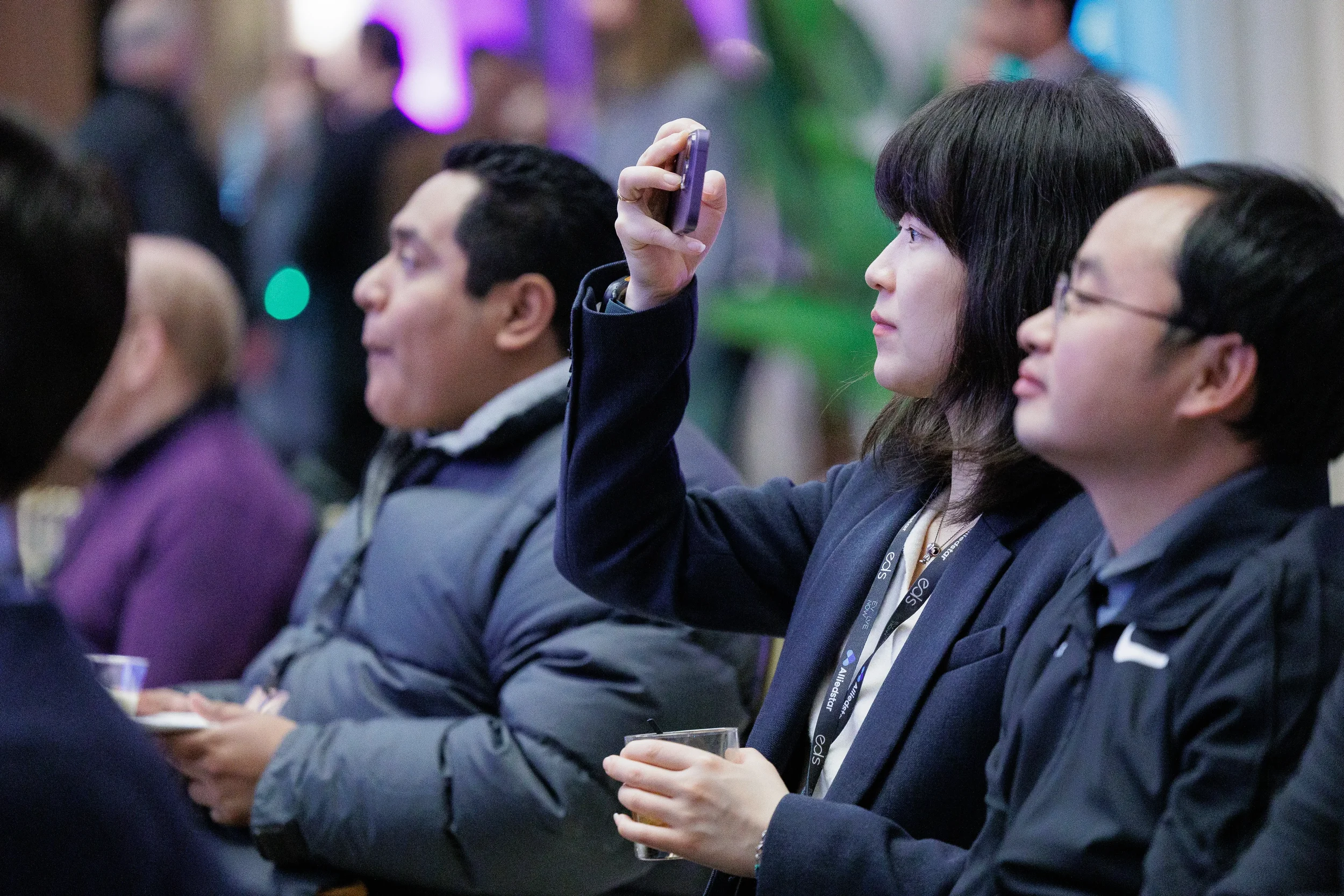 Lanyard-wearing attendee raises phone to photograph stage during Orlando industry conference