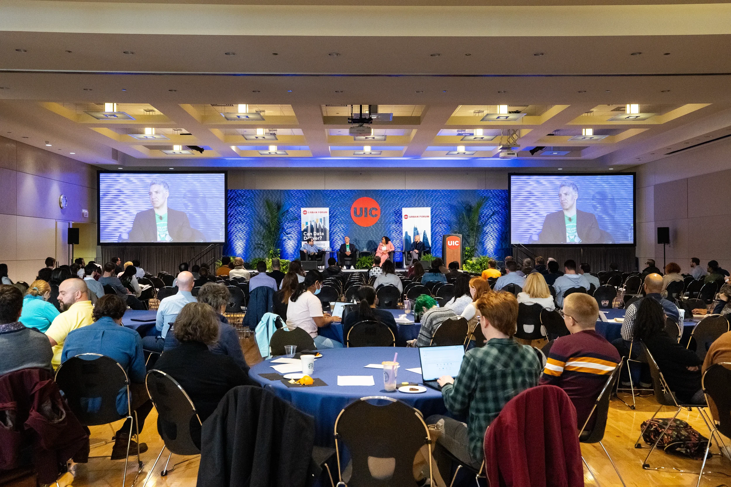 Wide view of seated audience watching panel discussion on screens at Chicago conference