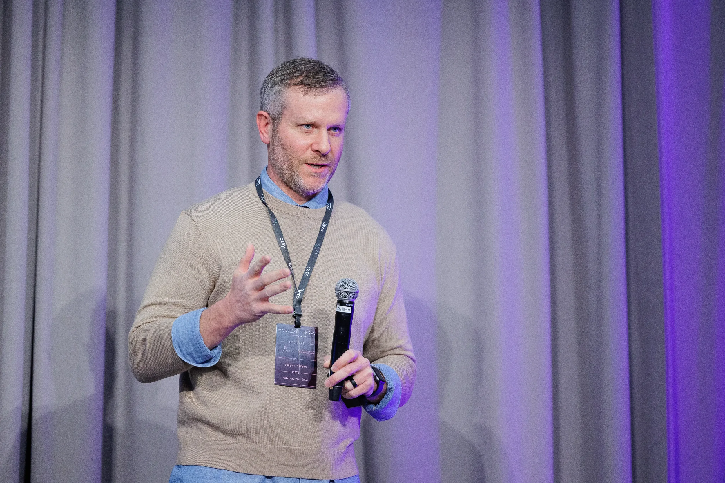 Speaker wearing lanyard badge gestures with microphone on stage at Chicago industry networking event