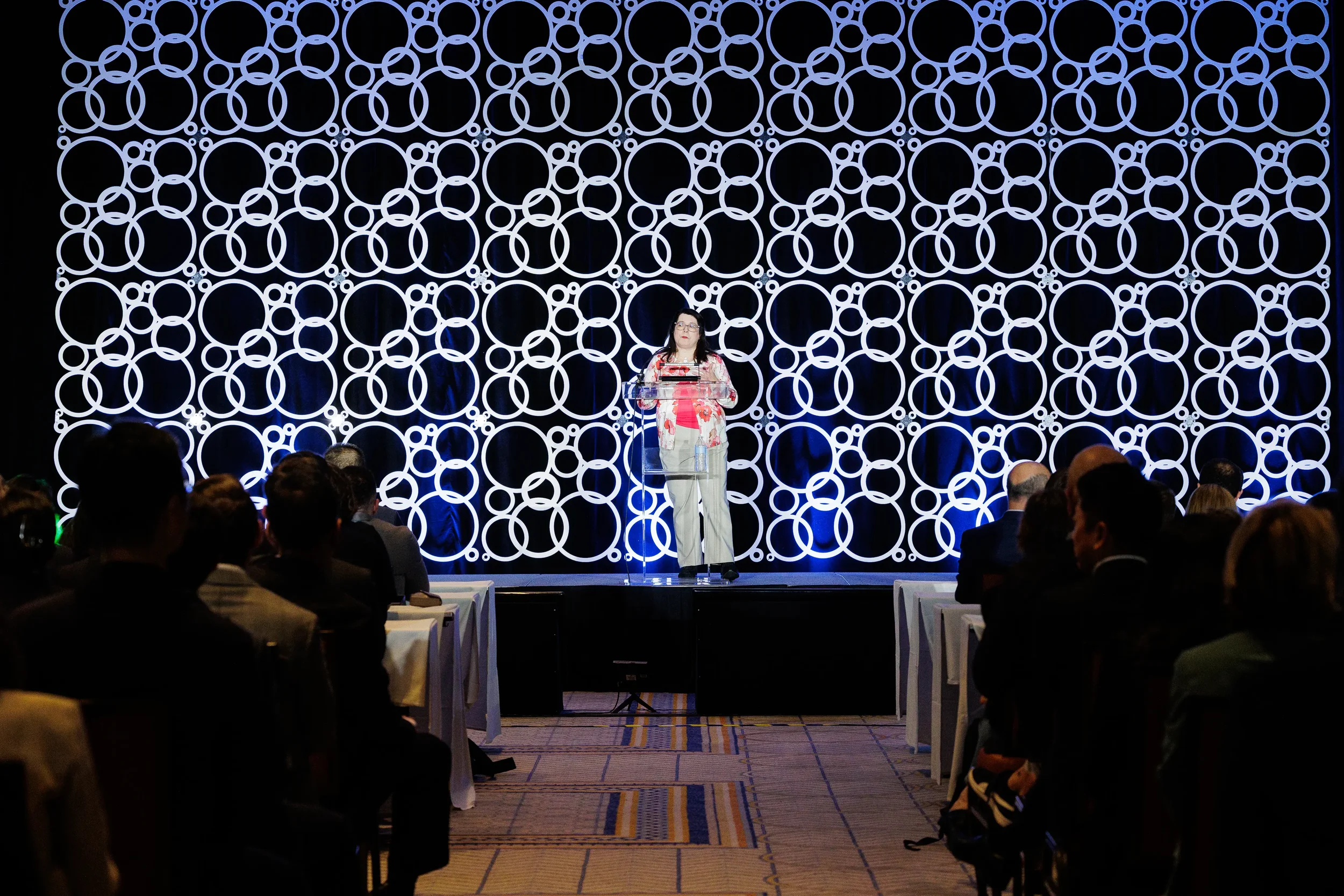 Speaker addresses audience from podium with circular backdrop in Chicago ballroom