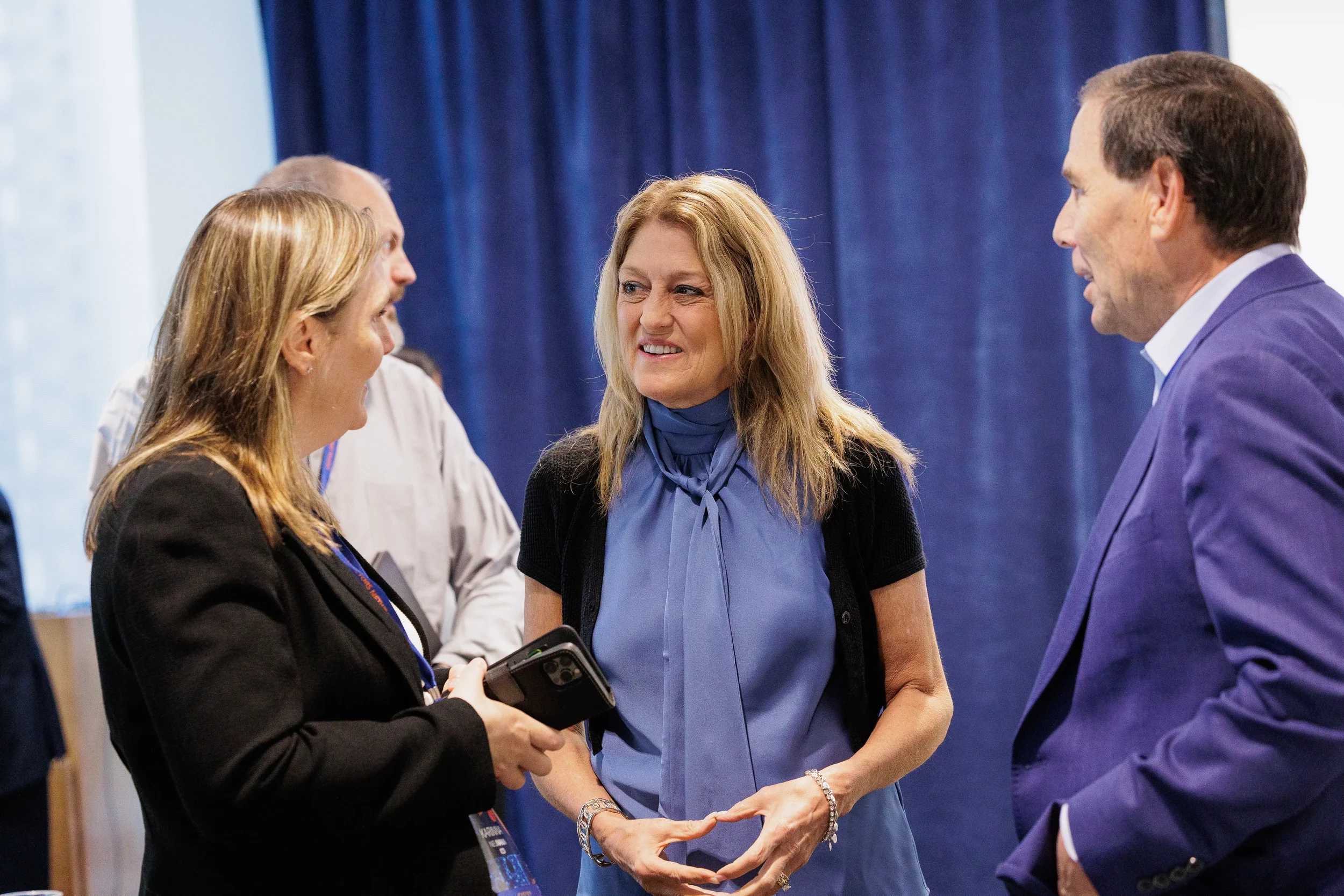 Three attendees with lanyards smile and converse during networking break at Chicago corporate conference