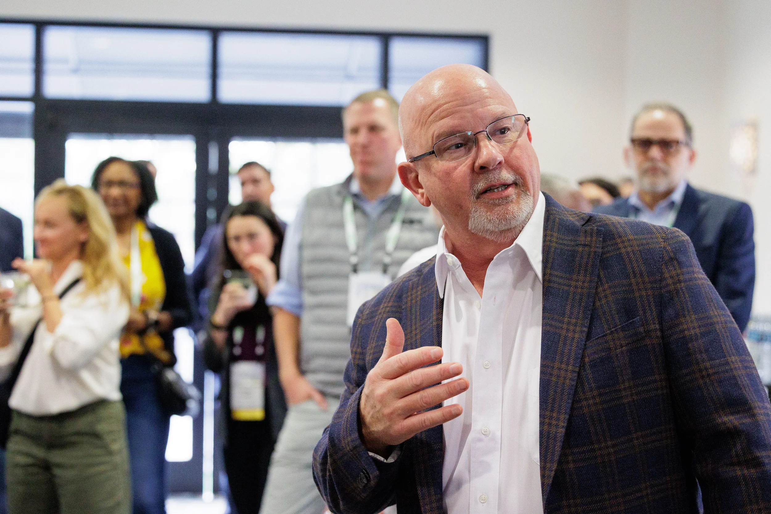 Suited speaker gestures to gathered crowd of attendees in foyer at Orlando industry conference