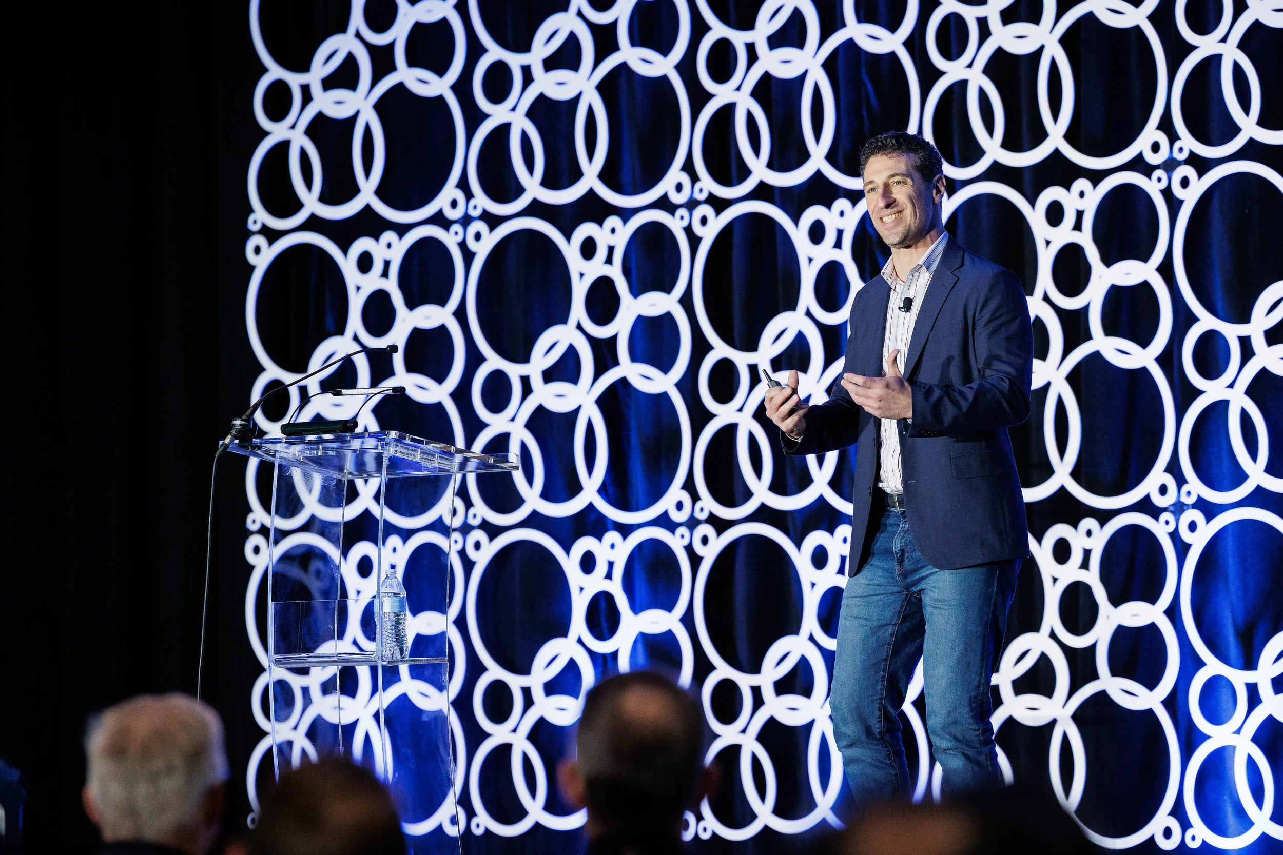 Smiling speaker in blue blazer presents beside clear podium on stage at Orlando industry conference
