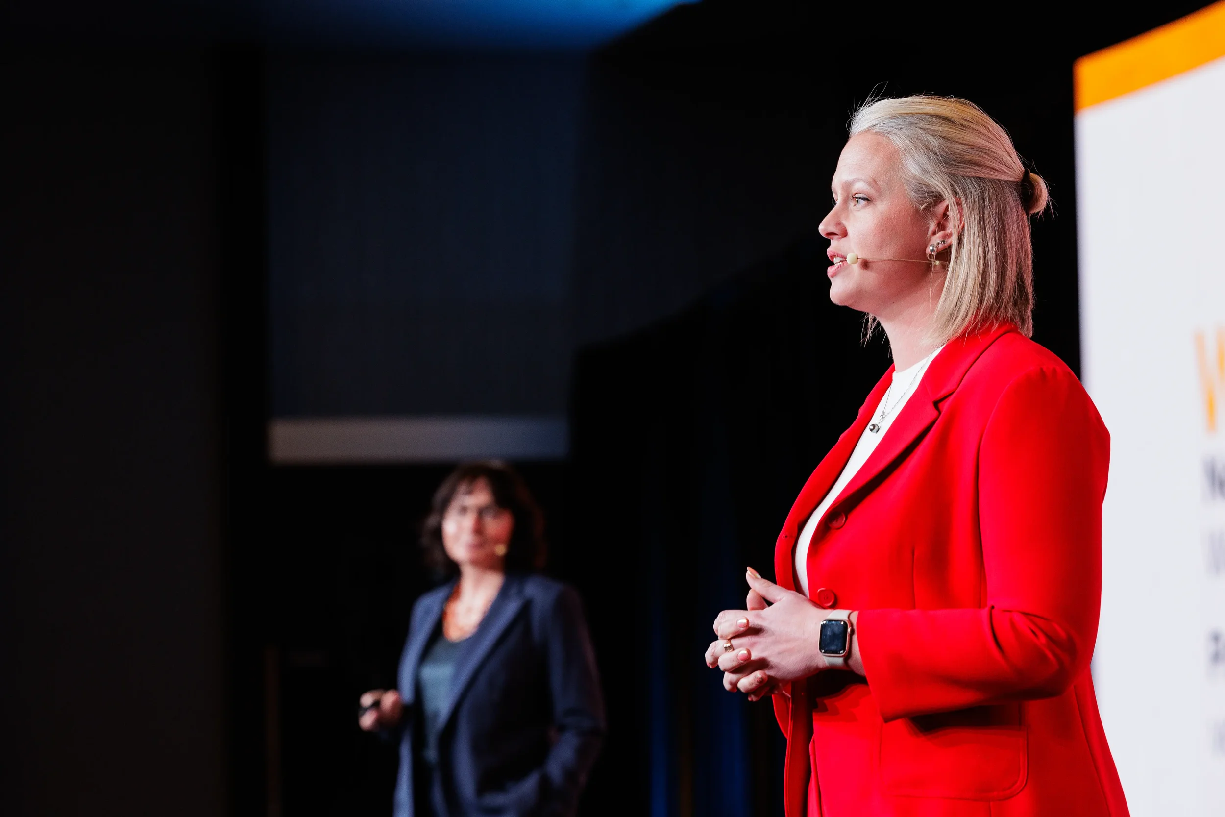 Speaker in red blazer presents with headset microphone on stage at Orlando corporate event