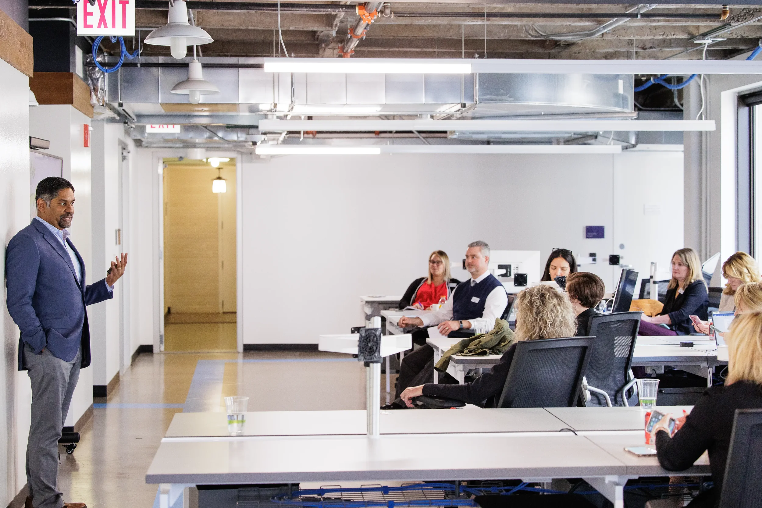Male speaker gestures while addressing a small seated group in a modern workspace at Orlando conference