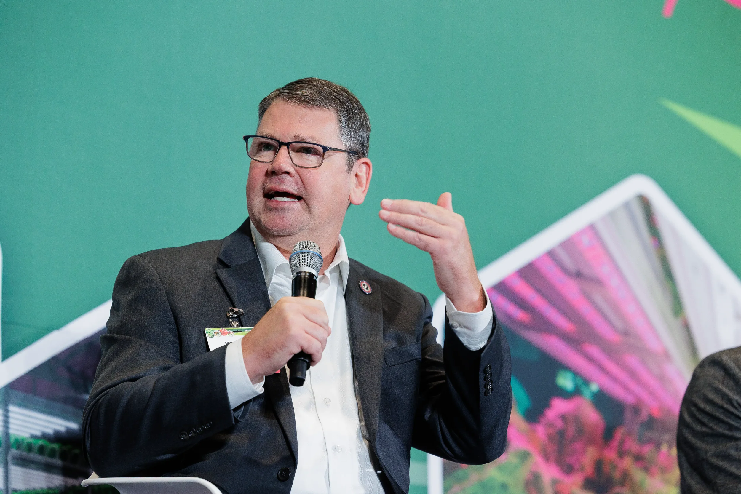 Panelist speaks into microphone with hand raised in front of branded green backdrop at Orlando industry conference
