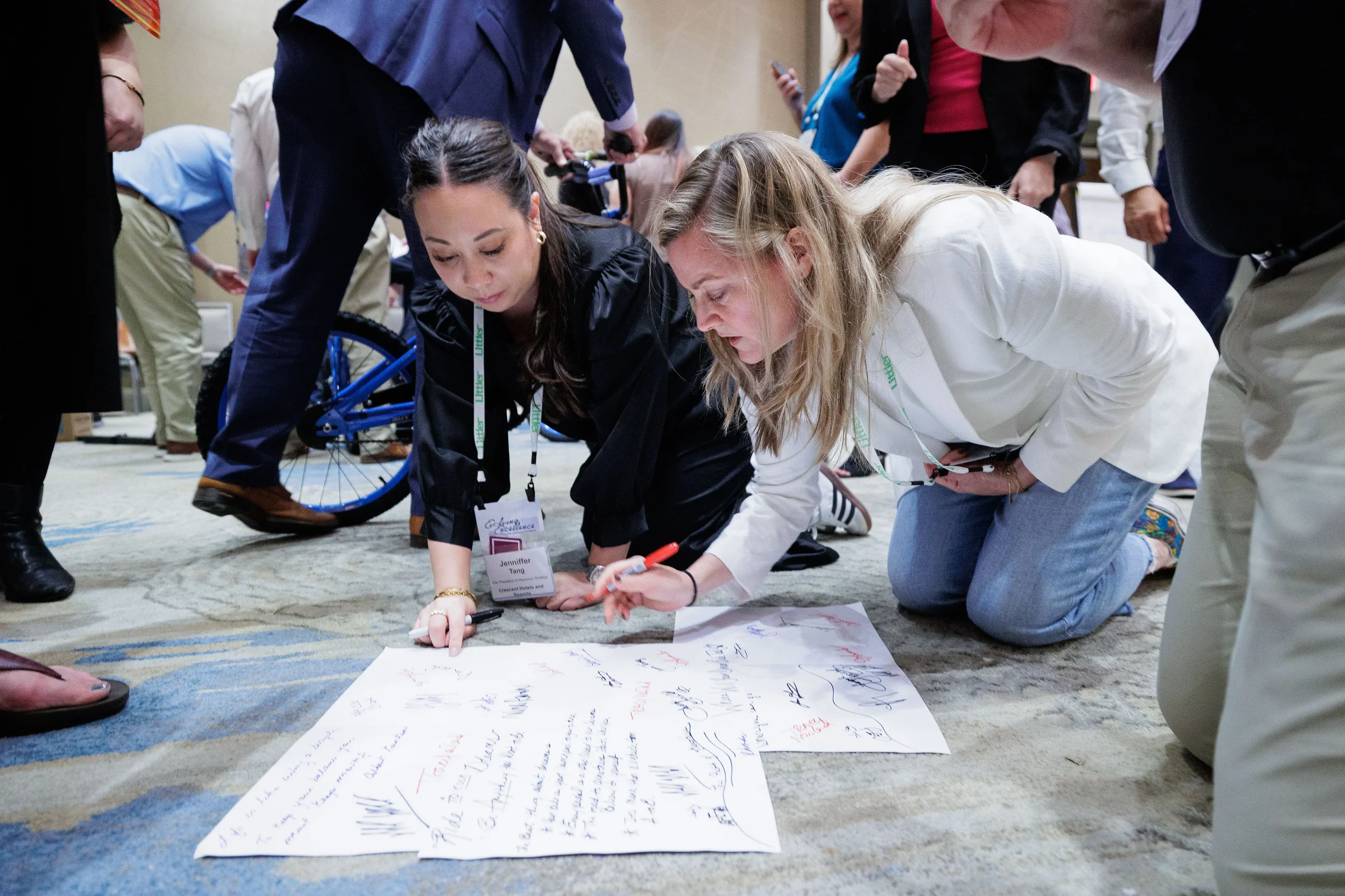 Two female attendees with lanyards kneel on floor writing during team building activity at Chicago corporate conference